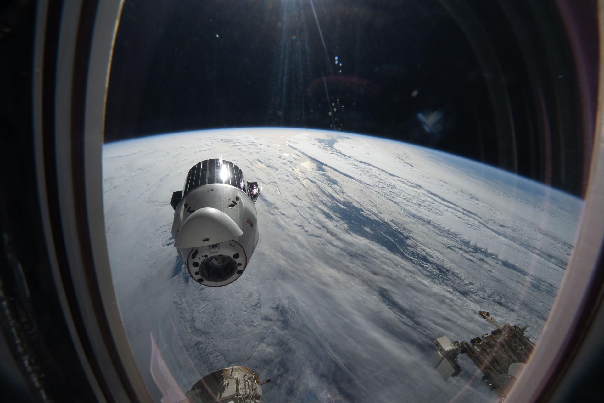 A SpaceX Dragon cargo spacecraft backs away from the International Space Station moments after undocking from the Harmony module's forward port while orbitng 265 miles above a cloudy North Pacific Ocean. Dragon, packed with completed science experiments and cargo for retrieval and analysis on Earth, parachuted to a splashdown off the coast of southern California the following day,