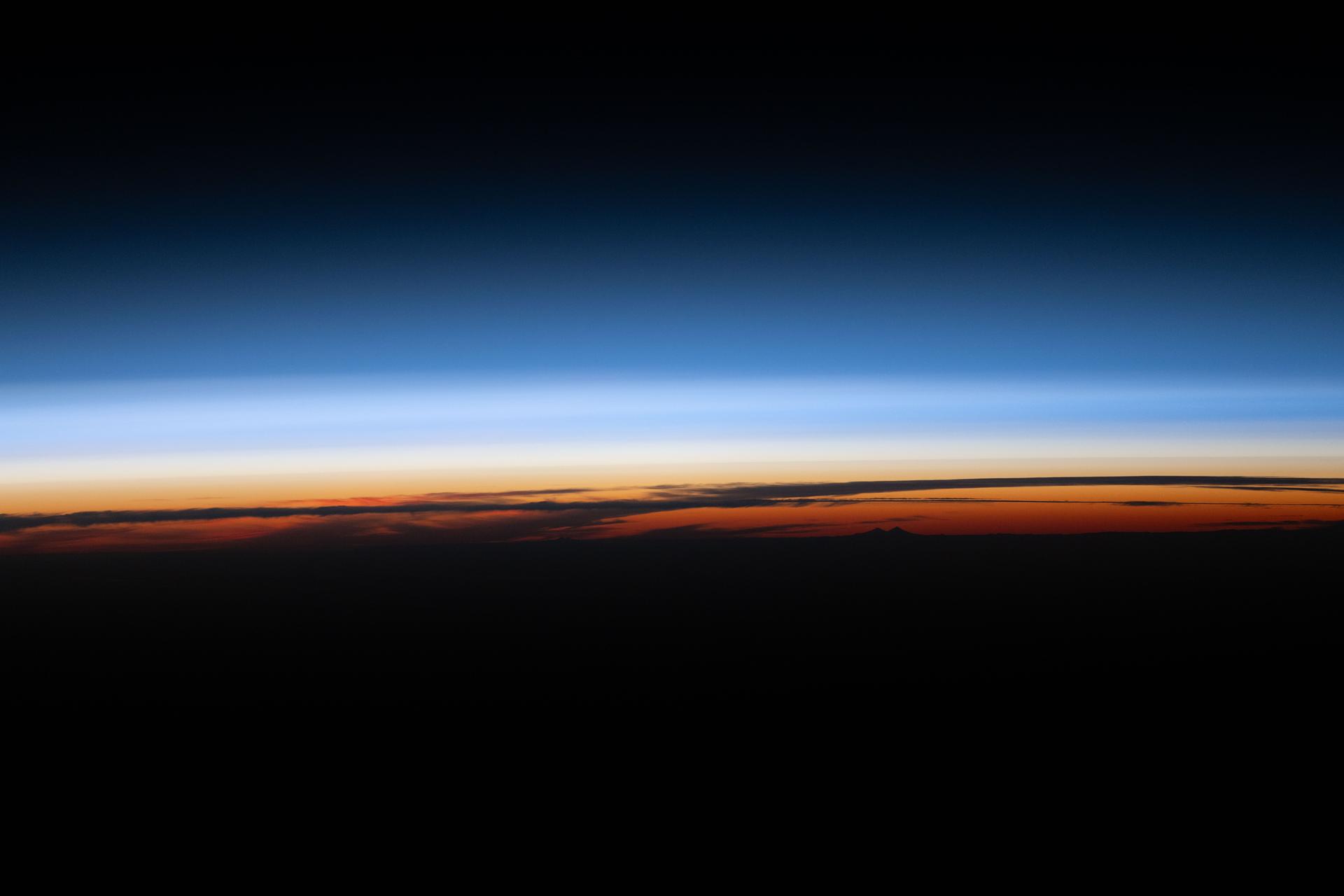 A sunset below Earth’s horizon silhouettes the clouds and illuminates the atmosphere in orange and blue hues, contrasting the planet’s darkened surface with the blackness of outer space. The International Space Station was orbiting 270 miles above the South Atlantic Ocean, off the coast of Argentina, at approximately 6:53 p.m. local time.