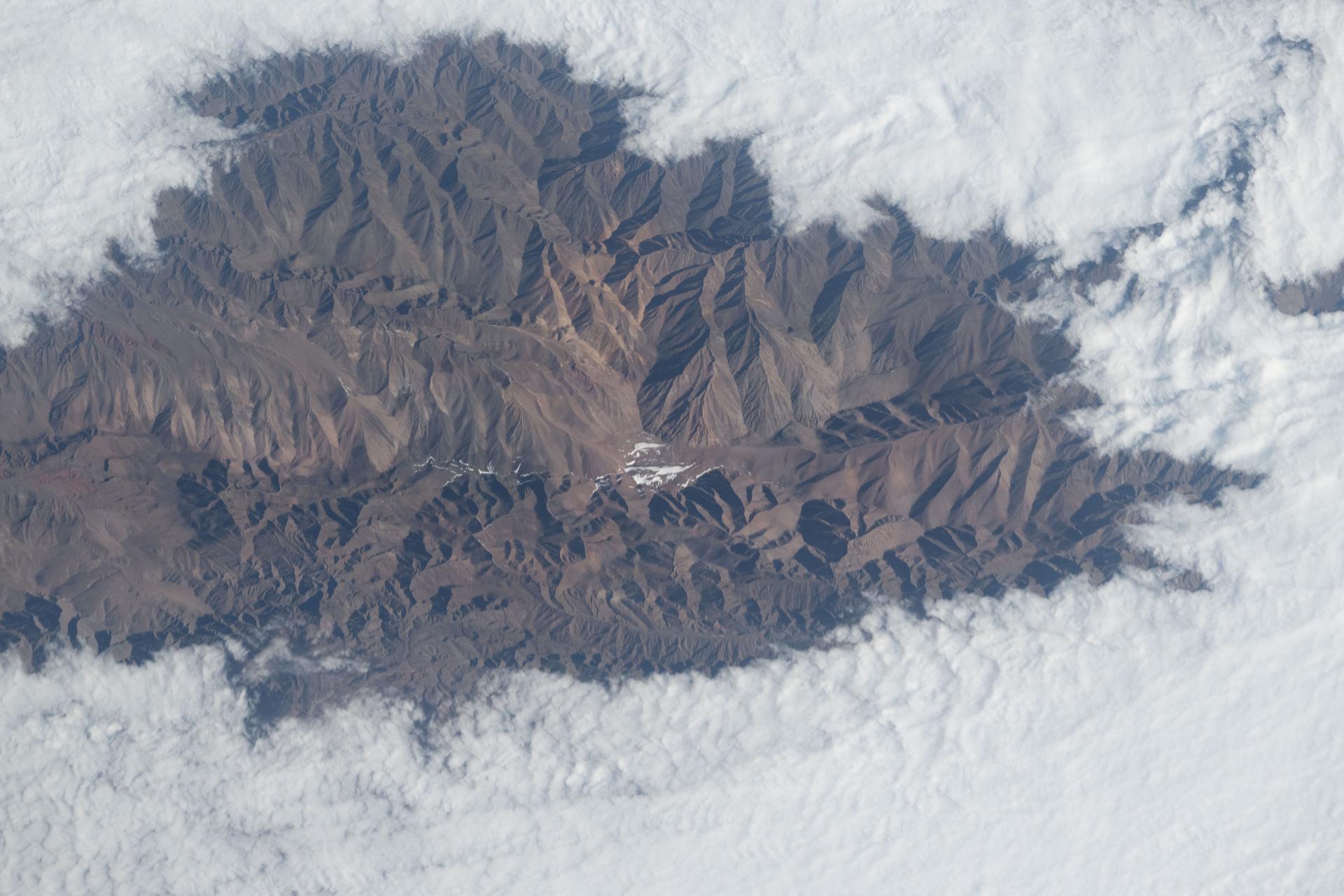 Clouds surround the rugged peaks of the Andes mountain range in this photograph taken from the International Space Station as it orbited 264 miles above Argentina. The dramatic contrast between the sharp mountaintops and the shifting cloud layers highlights the region’s dynamic weather patterns and diverse terrain.