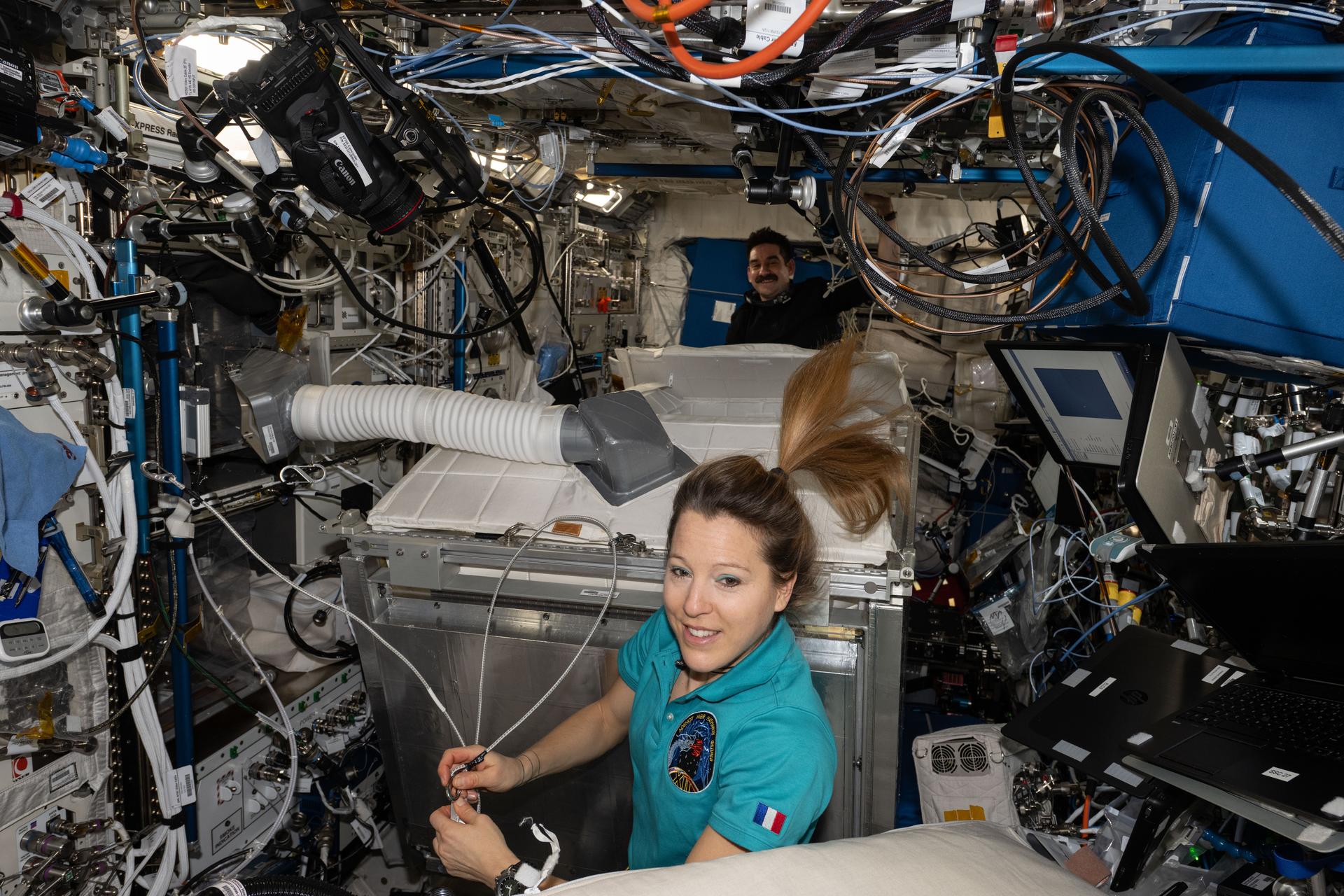 Expedition 74 flight engineers Sophie Adenot of ESA (European Space Agency) and Jack Hathaway of NASA (background) are pictured inside the International Space Station's Columbus laboratory module. The astronauts were upgrading a temporary sleep station, also called the Crew Alternate Sleep Accommodation (CASA), aboard Columbus. CASA modifications include a better fit for crew members, improved airflow velocity, an updated lighting configuration, and upgraded side panels and interior liners.