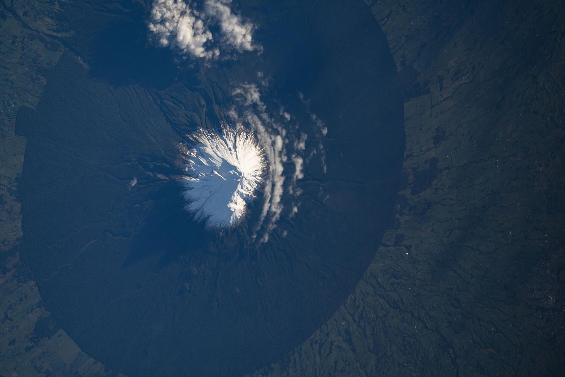Mount Taranaki, a dormant stratovolcano in New Zealand that last erupted in 1854, sits inside Egmont National Park, which is bounded by a six‑mile radius that protects a forest reserve forming its geological circular base. The International Space Station was orbiting 266 miles above the Tasman Sea at the time of this photograph.