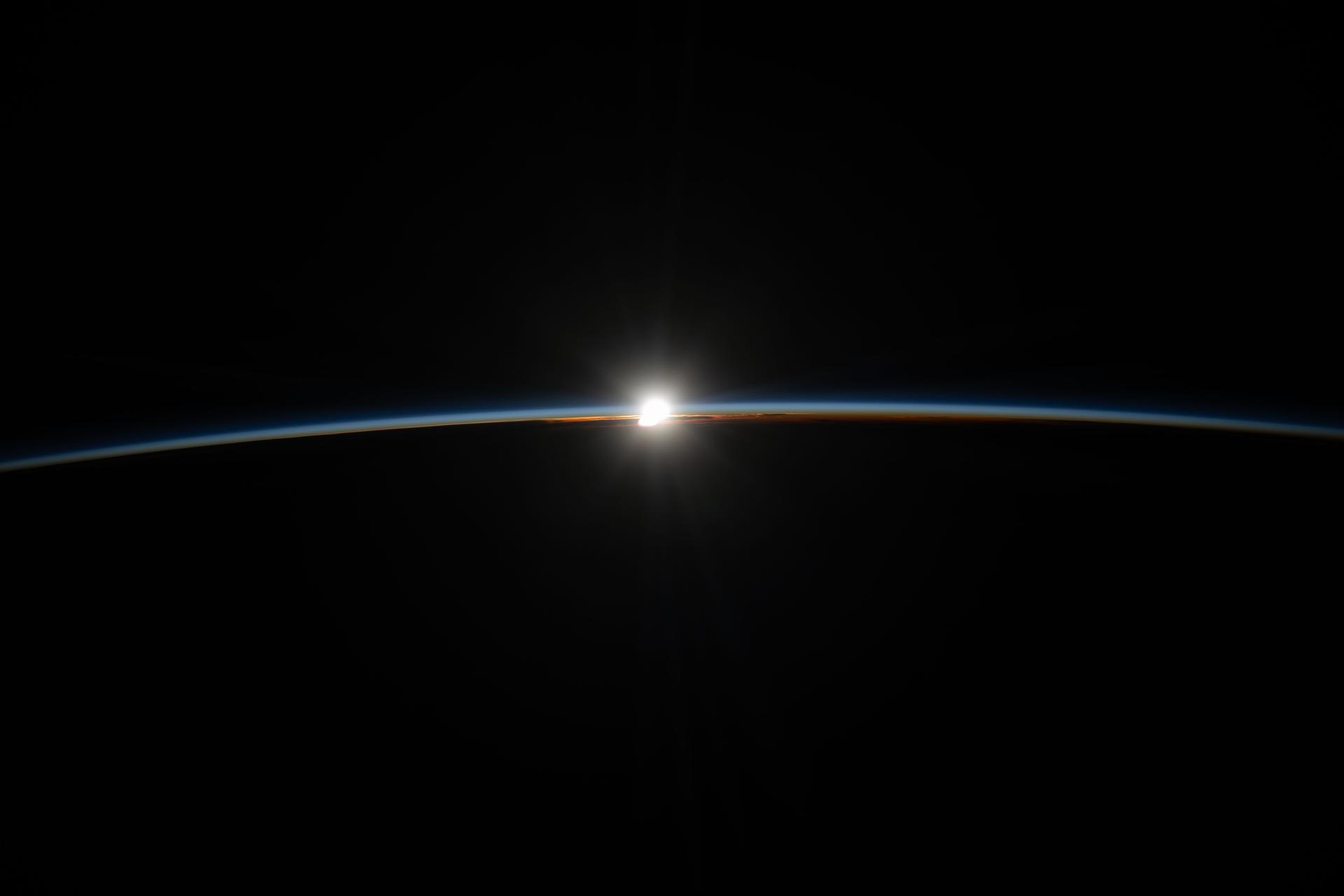 A diamond‑like orbital sunset, also known as a sun glint, flares briefly, illuminating Earth’s thin atmosphere with fading orange and blue hues that outline the horizon. The International Space Station was orbiting 265 miles above the far eastern China–Russia border at approximately 12:48 a.m. local time when this photograph was taken.