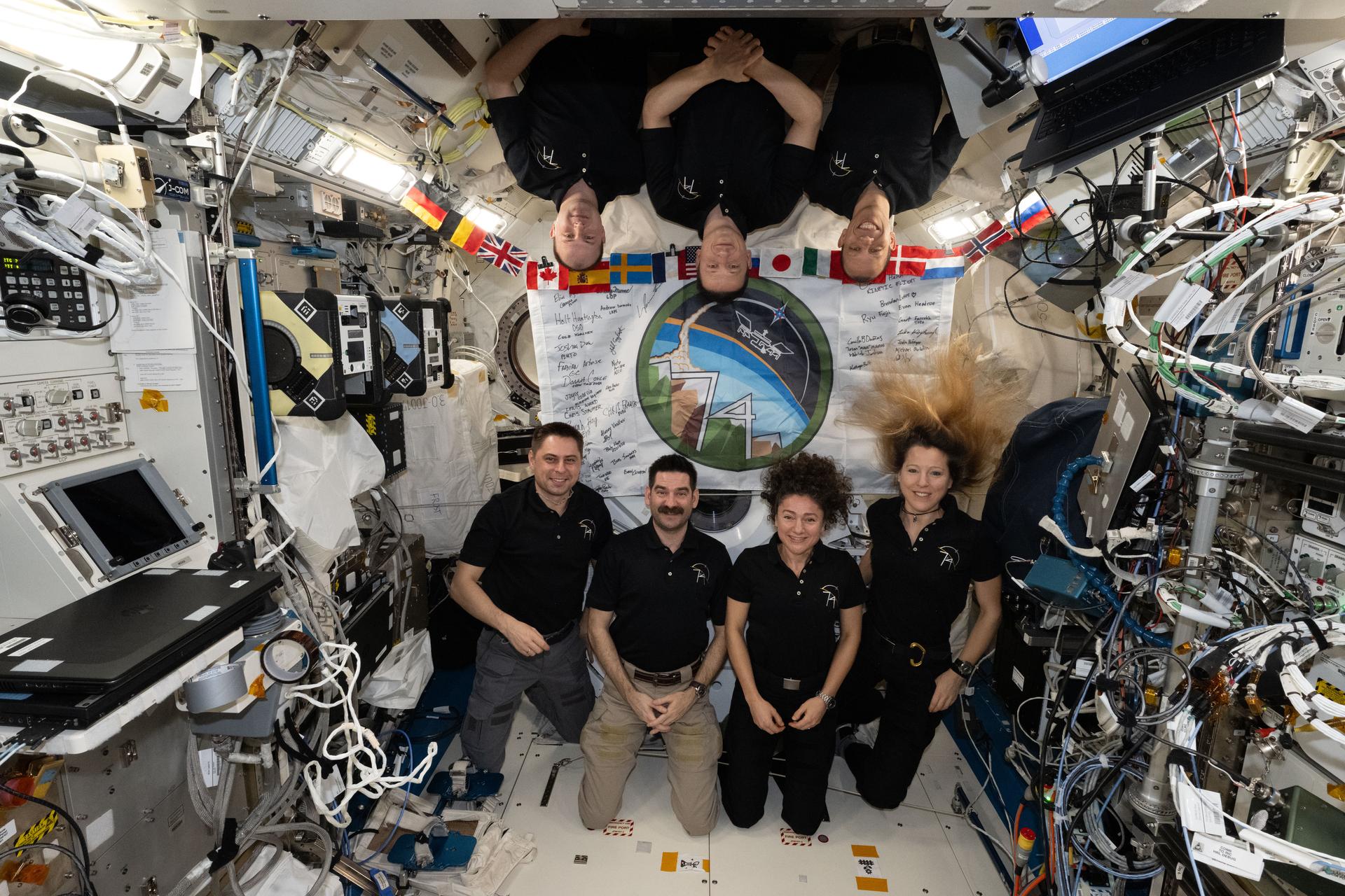 The seven‑member Expedition 74 crew poses for a portrait inside the International Space Station’s Kibo laboratory module. At bottom left are Roscosmos cosmonaut Andrey Fedyaev, NASA astronauts Jack Hathaway and Jessica Meir, and ESA (European Space Agency) astronaut Sophie Adenot. At top are Roscosmos cosmonauts Sergei Mikaev and Sergey Kud‑Sverchkov, along with NASA astronaut Chris Williams. In the background is a flag with the Expedition 74 insignia, sent to the orbital outpost and decorated with signatures from mission controllers on the ground.