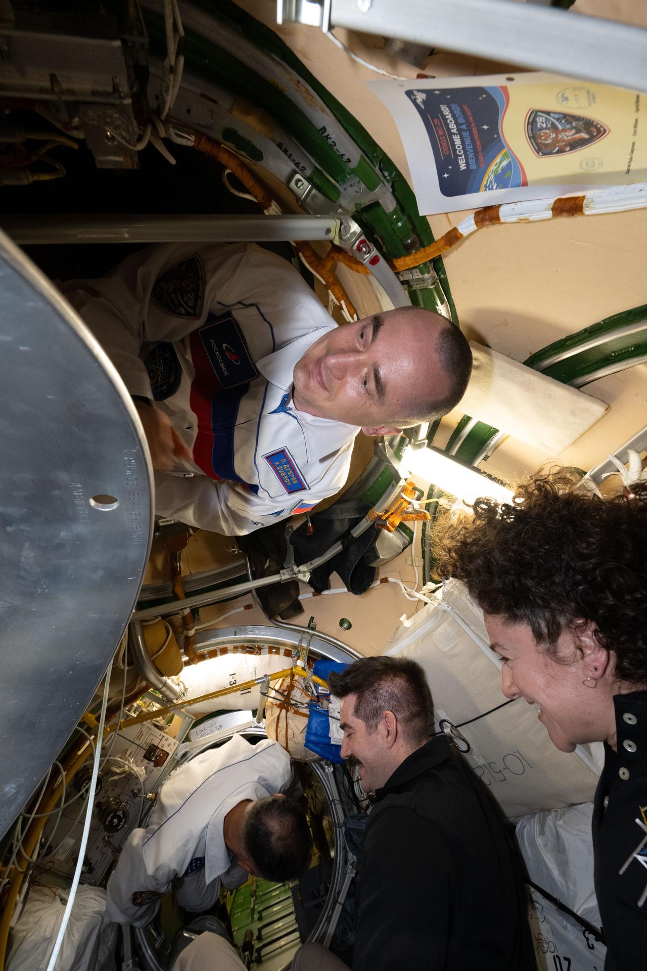 Roscosmos cosmonaut Pyotr Dubrov (top) and NASA astronaut Anil Menon (bottom) enter the International Space Station with Roscosmos cosmonaut Anna Kikina (out of frame) shortly after docking to the Prichal module inside the Soyuz MS-29 spacecraft. Welcoming the new crew members are Expedition 74 flight engineers Jack Hathaway and Jessica Meir, both NASA astronauts.