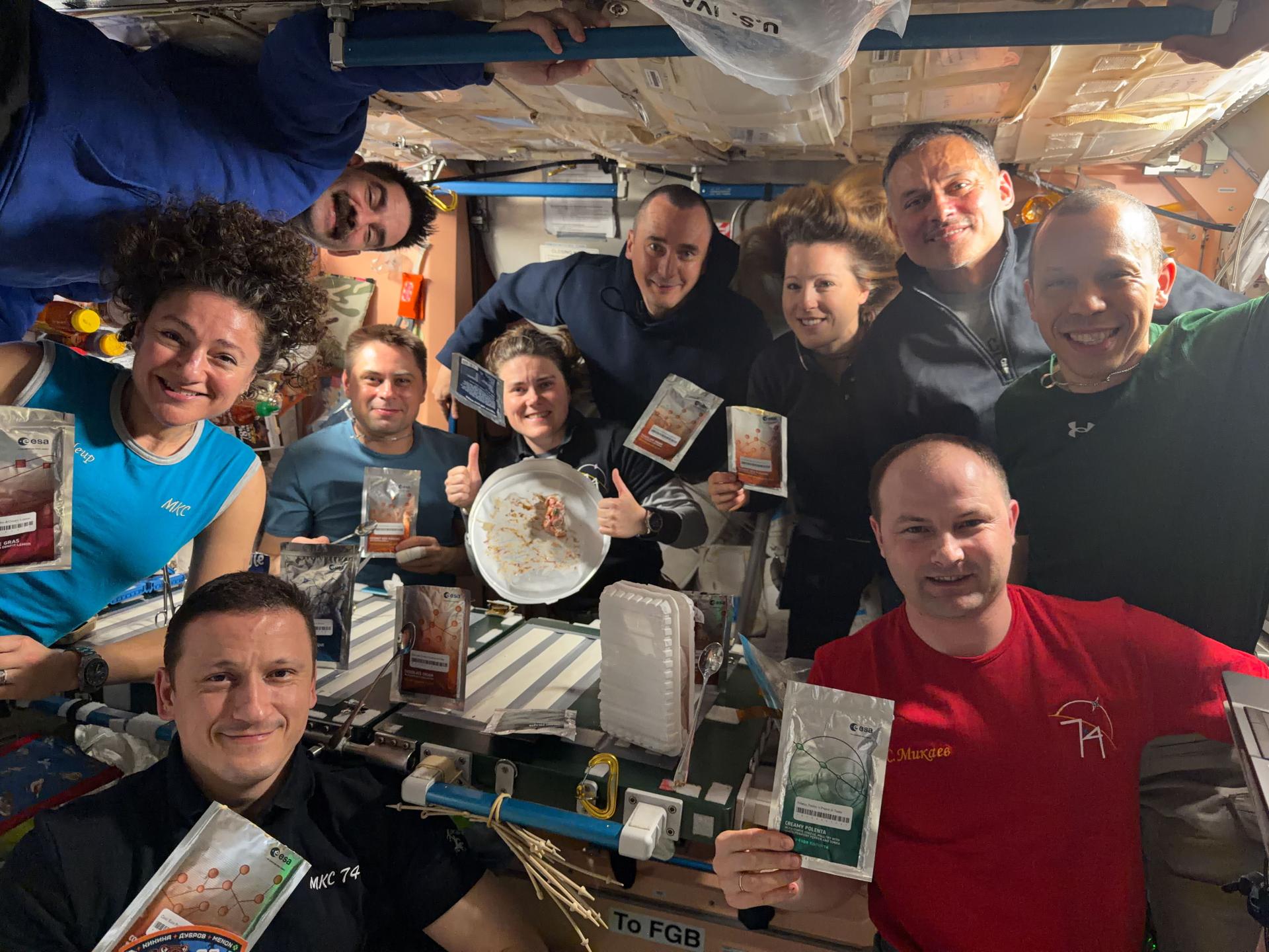 All ten International Space Station crew members gather inside the Unity module for a portrait during dinnertime, showing off gourmet food packages from the European Space Agency (ESA). Clockwise from bottom left are Roscosmos cosmonaut Sergey Kud-Sverchkov; NASA astronauts Jessica Meir and Jack Hathaway; Roscosmos cosmonauts Andrey Fedyaev, Anna Kikina, and Pyotr Dubrov; ESA astronaut Sophie Adenot; NASA astronauts Anil Menon and Chris Williams; and Roscosmos cosmonaut Sergei Mikaev.