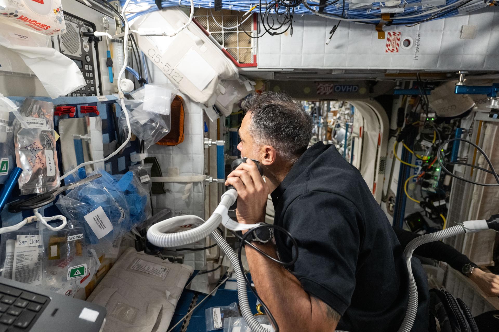 iss074e0831855 (July 23, 2026) --- NASA astronaut and Expedition 74 flight engineer Anil Menon gives himself a shave using an electric razor attached to a vacuum that collects loose clippings to keep the International Space Station’s atmosphere clean in microgravity. Credit: NASA/Chris Williams