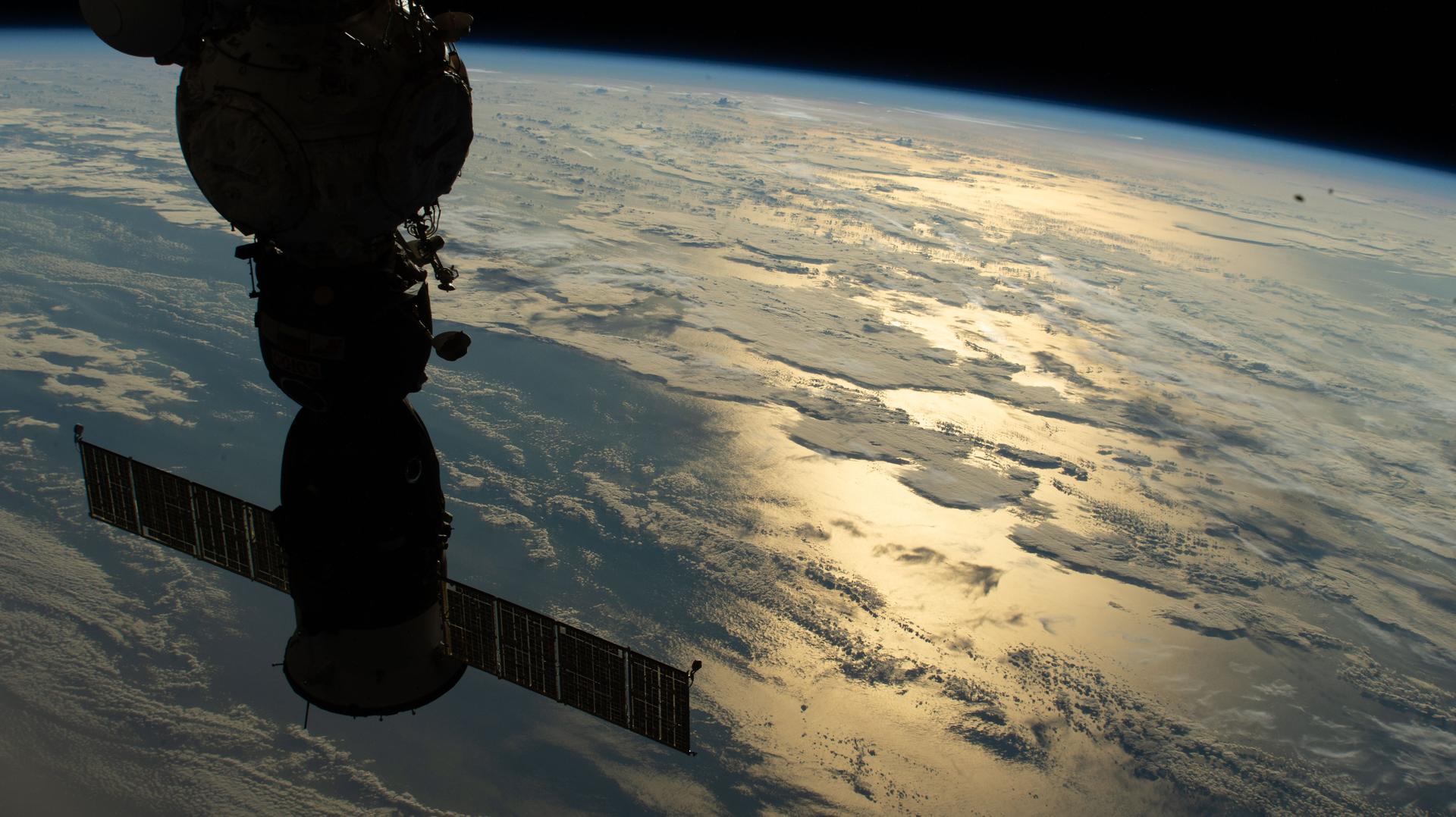 iss075e0002047 (Aug. 1, 2026) --- The Soyuz MS‑29 spacecraft, docked to the Prichal module, is silhouetted against the sun’s light glinting across the Atlantic Ocean in this photograph from the International Space Station as it orbited 264 miles above Earth. Credit: NASA
