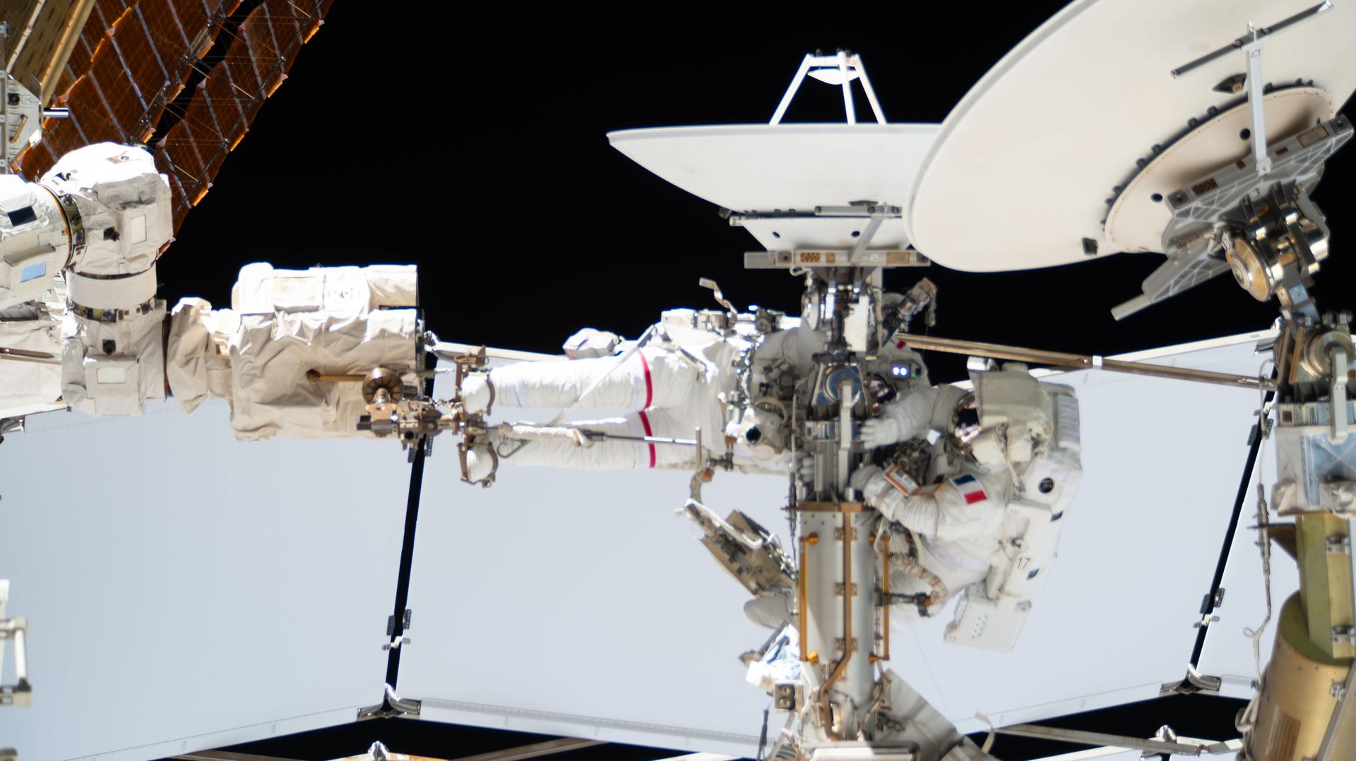 From left, Expedition 75 flight engineers Anil Menon of NASA (partially obscured and wearing the spacesuit with a red stripe on the legs) and Sophie Adenot of ESA (European Space Agency) work together during a six‑hour and 23‑minute spacewalk outside the International Space Station. The duo disconnected a failed high‑speed antenna and secured it with a long‑duration tie‑down on the orbital outpost’s Z1 truss segment. A spare antenna will be installed on the Z1 truss during a future spacewalk.