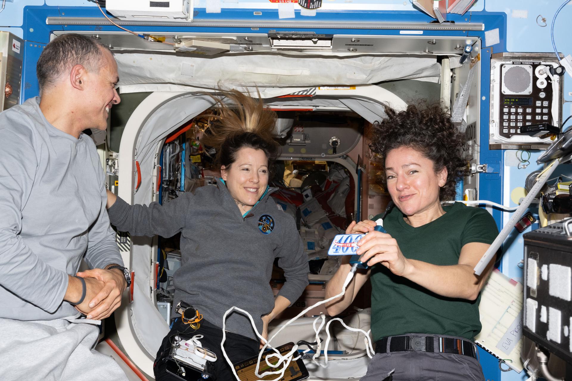 Expedition 75 flight engineers Anil Menon of NASA and Sophie Adenot of ESA (European Space Agency) and International Space Station commander Jessica Meir of NASA gather together inside the International Space Station's Destiny laboratory module. Meir is holding a patch given to her commemorating 400 cumulative days in space (and counting) across two missions to the orbital outpost.