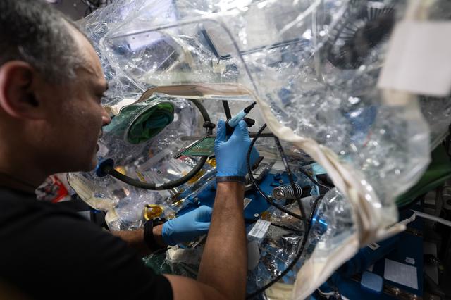 NASA astronaut Anil Menon solders components on a circuit board inside the International Space Station