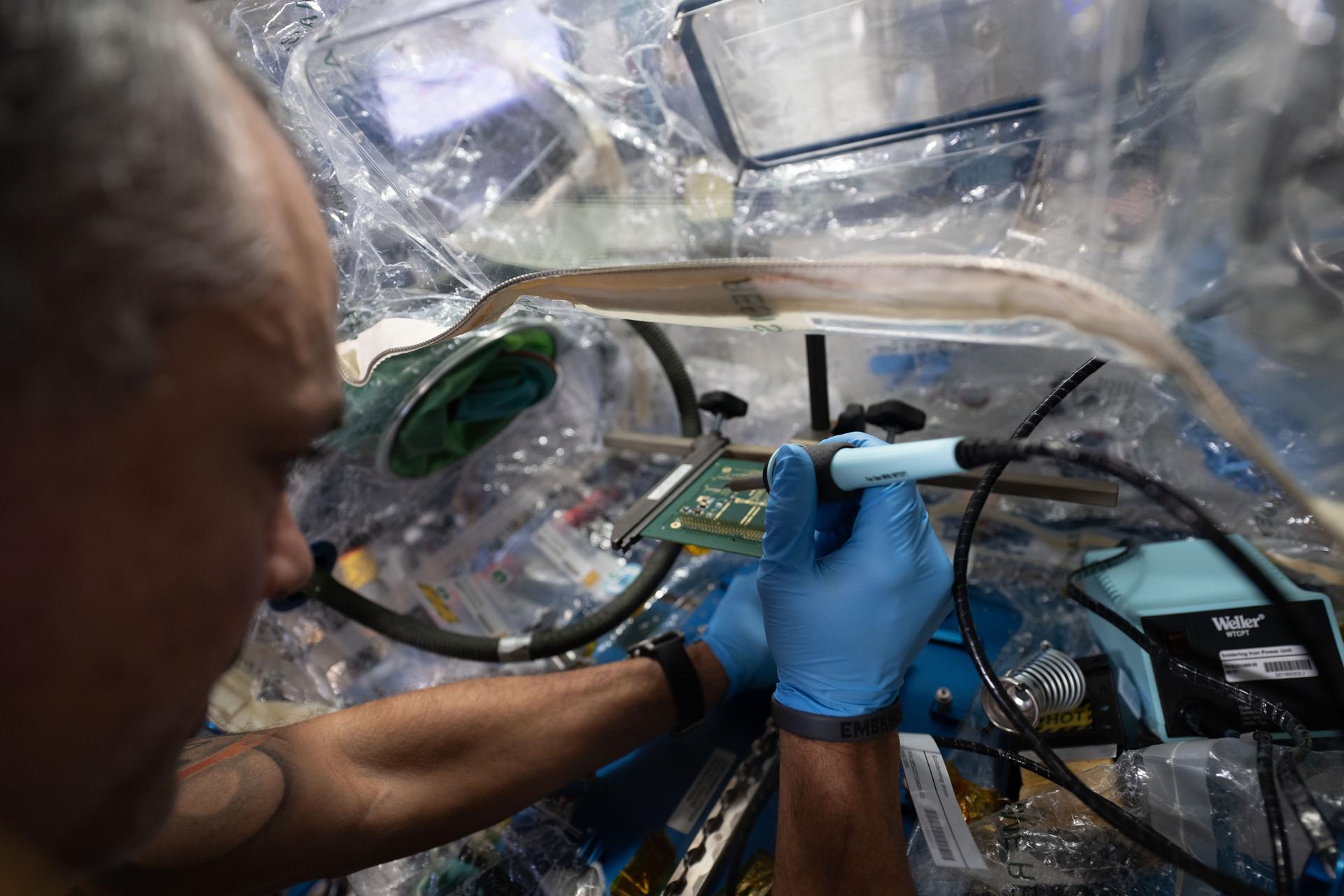 iss075e0103084 (Sept. 14, 2026) --- NASA astronaut and Expedition 75 flight engineer Anil Menon uses a lead-free soldering technique to solder components on a circuit board and demonstrate the manufacturing and repair of electronics in microgravity. Menon conducted safe research operations inside a container system attached to the Harmony module's maintenance work area to protect the International Space Station's atmosphere. The MIYOKA experiment will return the space-soldered samples to Earth for analysis and compare them to identical ground-soldered samples. Results may lead to reduced reliance on costly resupply missions. Credit: ESA/Sophie Adenot