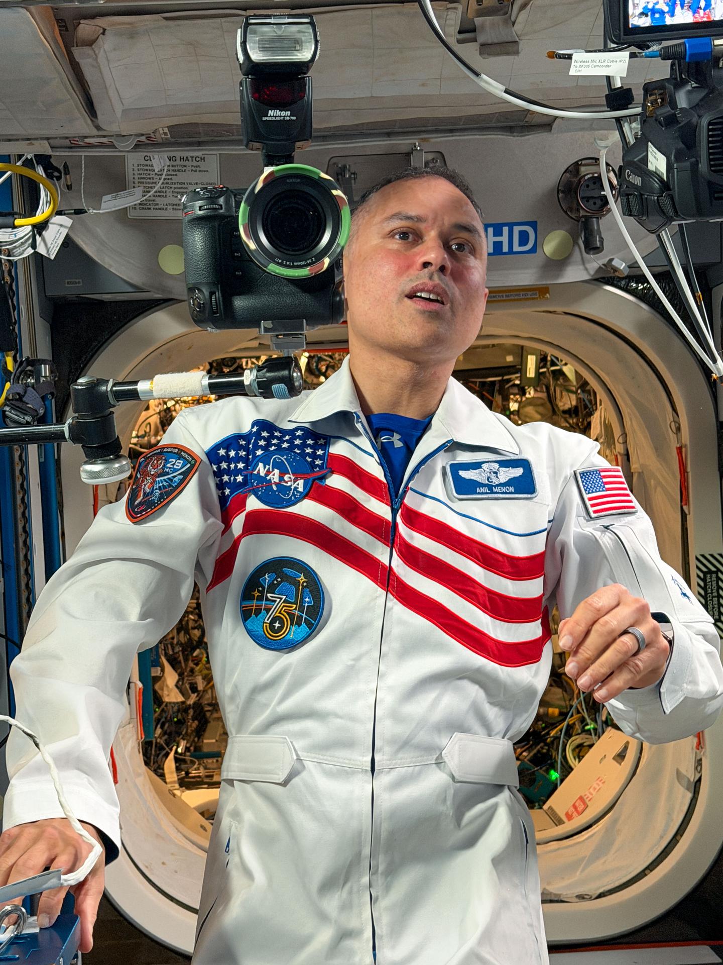 NASA astronaut and Expedition 75 flight engineer Anil Menon prepares to take a portrait of his fellow crewmates aboard the International Space Station while awaiting the arrival of NASA's SpaceX Crew‑13 mission and its four crew members.