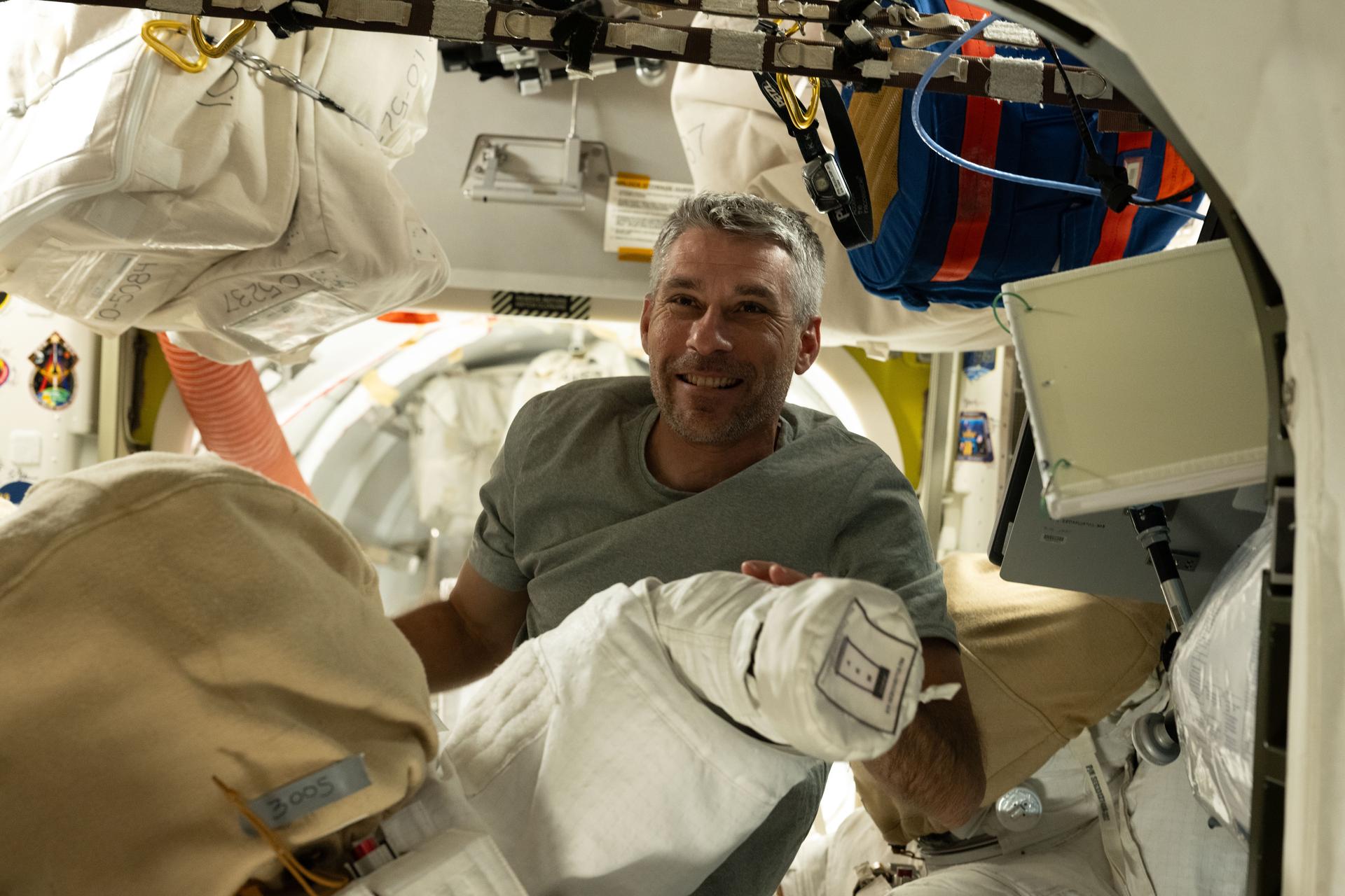 NASA astronaut and Expedition 75 flight engineer Luke Delaney smiles for a portrait while checking out a spacesuit inside the International Space Station's Quest airlock.