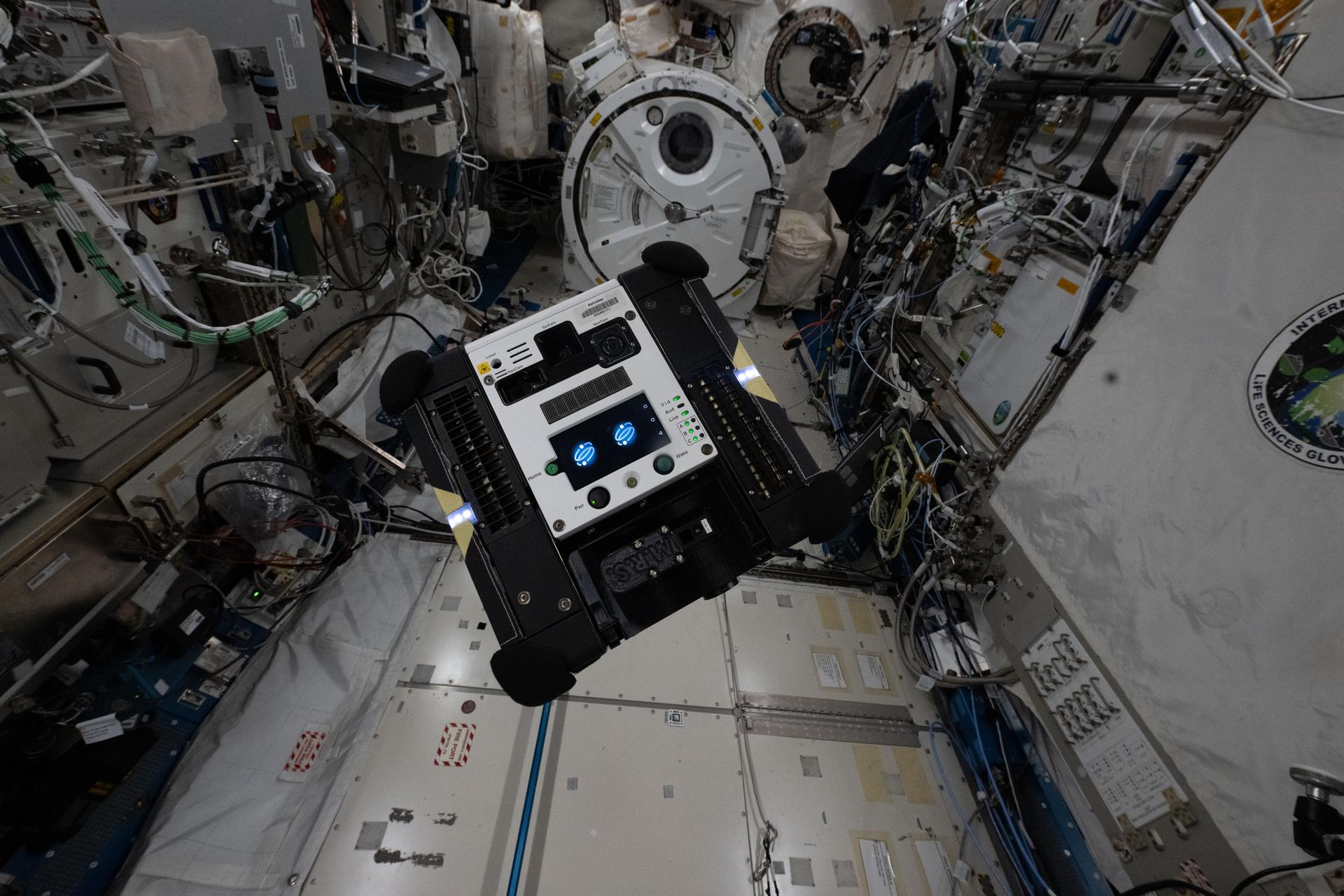 A toaster-sized Astrobee free-flying robotic assistant is pictured autonomously maneuvering inside the International Space Station's Kibo laboratory module. The cube-shaped robot is designed to help scientists and engineers develop and test technologies for use in microgravity, assist astronauts with routine chores, and provide ground controllers with additional eyes and ears aboard the orbital outpost.