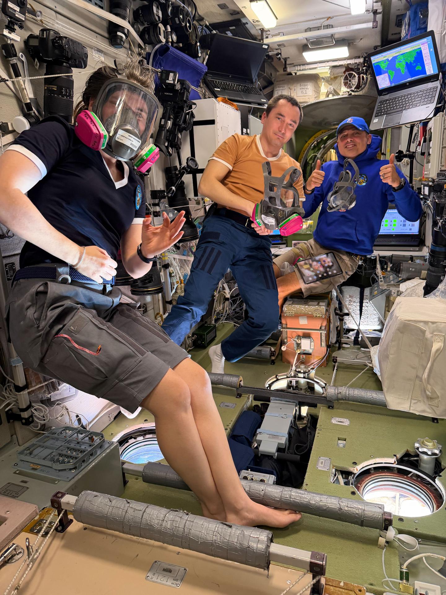 From left, Expedition 75 crewmates Anna Kikina and Pyotr Dubrov of Roscosmos and Anil Menon of NASA train to wear and use an emergency breathing mask inside the International Space Station's Zvezda service module. Each crew member ensures the mask fits, seals properly, and can be used quickly and safely in the unlikely event of an emergency involving harmful gas.