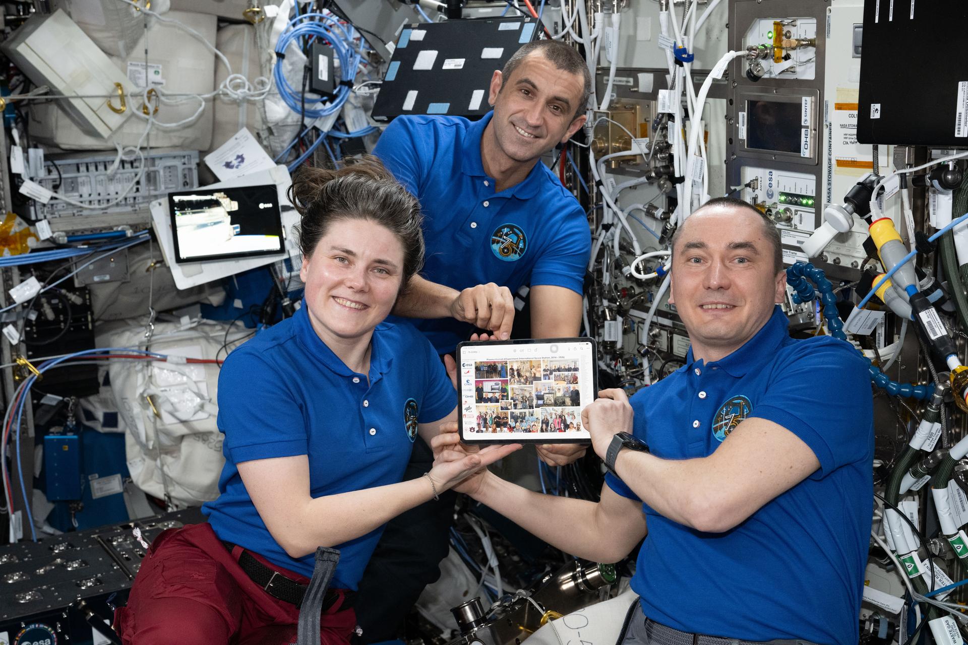 From left, Expedition 75 flight engineers Anna Kikina and Sergey Teteryatnikov and station commander Pyotr Dubrov, all Roscosmos cosmonauts, pose for a portrait inside the International Space Station’s Columbus laboratory module. The trio show off a portrait of the ground personnel who supported the Plasma Crystal‑4 investigation. The microgravity physics study explored complex plasmas—mixtures of ionized gas, neutral gas, and microscopic particles that become highly charged, interact strongly with one another, and may form plasma crystals. Results may influence the design of future spacecraft and lead to new research methods.