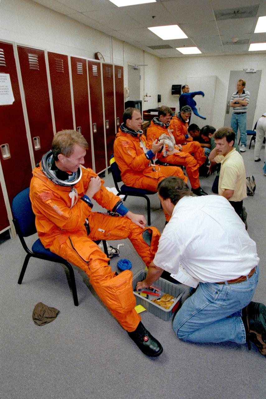 JSC2000-04751 (15 June 2000) --- Members of the STS-97 crew don training versions of the ascent and entry suits for a training session in the Johnson Space Center's Systems Integration Facility. Wearing the burnt-orange pressure suits, from the left, are astronauts Brent W. Jett, mission commander; Michael J. Bloomfield, pilot; and Joseph R. Tanner and Marc Garneau, both mission specialists. Garneau represents the Canadian Space Agency (CSA). Suit technicians assisting are Mike Birkenseher, Brad Milling, Steve Clendenin and Rudy Molina. In the background Carlos I. Noriega, mission specialist, prepares to put on his suit with the assistance of suit tech John Hazelhurt.