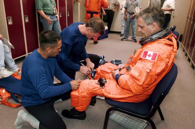 JSC2000-E-23527 (October 2000) --- Astronaut Marc Garneau, mission specialist representing the Canadian Space Agency (CSA), looks on as two crew mates assist him with final touches of suit-donning prior to a training session in the Johnson Space Center's Systems Integration Facility. Helping out are  astronauts Carlos I. Noriega (left) and  Joseph R. Tanner, mission specialists.