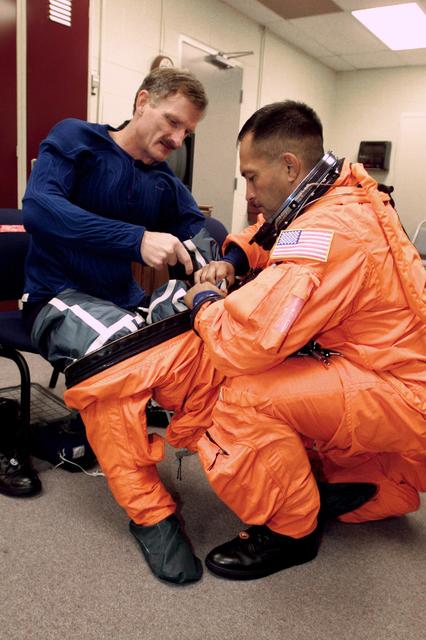 JSC2000-E-23530 (October 2000) --- Astronaut Joseph R. Tanner receives a helping hand from astronaut Carlos I. Noriega as the two STS-97 mission specialists don training versions of their pressure ascent and entry garments. The two were about to participate in a simulation of various parts of their scheduled November mission aboard the Space Shuttle Endeavour.