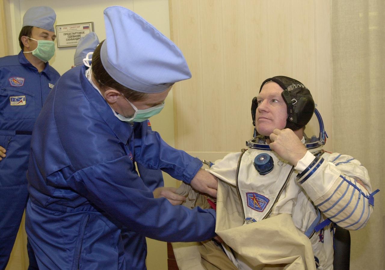 JSC2000-E-27082 (20 October 2000) --- Expedition 1 commander William M. (Bill) Shepherd gets help with his Sokol suit prior to a simulation at Baikonur.  Out of frame are Soyuz pilot Yuri P. Gidzenko and flight engineer Sergei K. Krikalev.