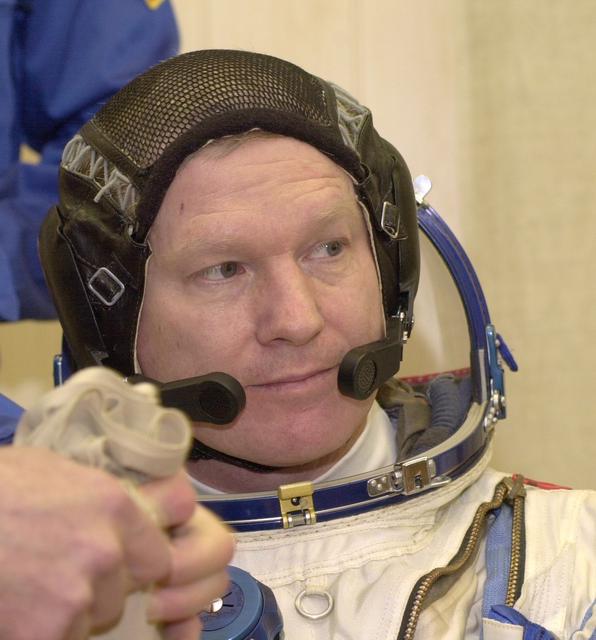 JSC2000-E-27083 (20 October 2000) --- Expedition 1 commander William M. (Bill) Shepherd gets help with his Sokol suit prior to a simulation at Baikonur.  Out of frame are Soyuz pilot Yuri P. Gidzenko and flight engineer Sergei K. Krikalev.