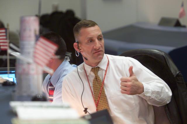 JSC2002-E-08143 (1 March 2002) ---  Astronaut Charles O. Hobaugh, seated at the Spacecraft Communicator (CAPCOM) console in the Shuttle Flight Control Room of the Johnson Space Center's Mission Control Center, gives a thumbs up signal, obviously connected to improving weather at the launch site for the Space Shuttle Columbia several hundred miles away in Florida. Astronaut William A. Oefelein is partially obscured in the background.