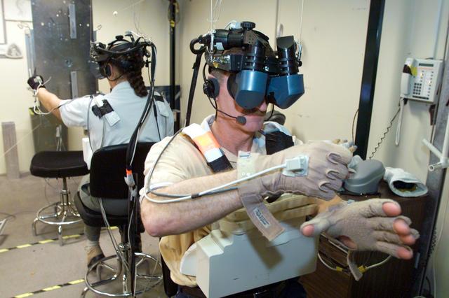 JSC2002-E-51051 (16 December 2002) --- Astronauts Joseph R. (Joe) Tanner (foreground) and Heidemarie M. Stefanyshyn-Piper, both STS-115 mission specialists, use virtual reality hardware in the Space Vehicle Mockup Facility at the Johnson Space Center (JSC) to rehearse some of their duties on the upcoming mission to the International Space Station (ISS). This type of virtual reality training allows the astronauts to wear a helmet and special gloves while looking at computer displays simulating actual movements around the various locations on the station hardware with which they will be working.