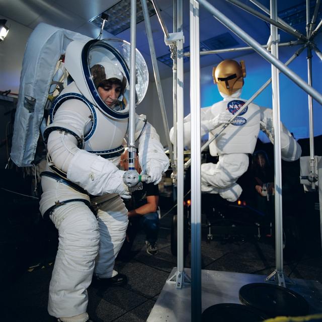 Photographic documentation of Robonaut activities involving joint task operations with a EVA suited astronaut (Nancy Currie) in bldg 9N,rm 1113 (Robonaut lab). Close-up view of Currie (in her EMU) working with the Robonauts (00299). Currie and one Robonaut work at a task .
