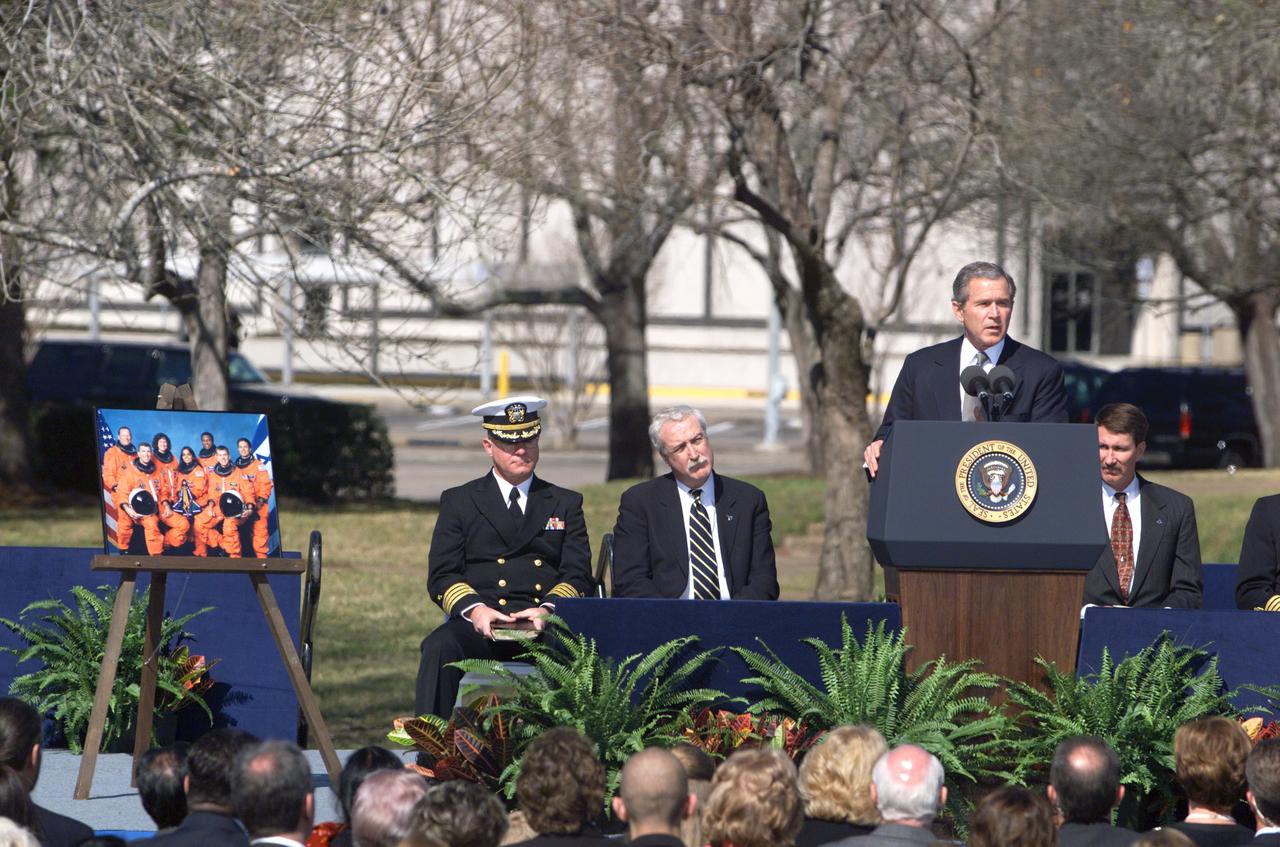 JSC2003-E-05938 (4 February 2003) --- President George W. Bush addresses the crowd on the mall of the Johnson Space Center during the memorial for the Columbia astronauts. Seated from the left are Captain Gene Theriot, Chaplain Corps (USN); NASA Administrator Sean O’Keefe; and astronaut Kent V. Rominger, Chief of the Astronaut Office. A portrait of the STS-107 Columbia crew is visible at left.