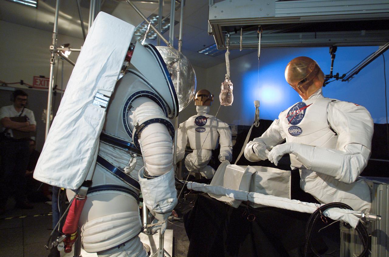 JSC2003-E-42632 (June 2003) --- Astronaut Nancy J. Currie, wearing an advanced concept space suit, participates in a test at the Johnson Space Center to evaluate hand-in-hand work with robots. The Robonaut pictured is one of two that were used in the demonstration's task -- the assembly of an aluminum truss structure.