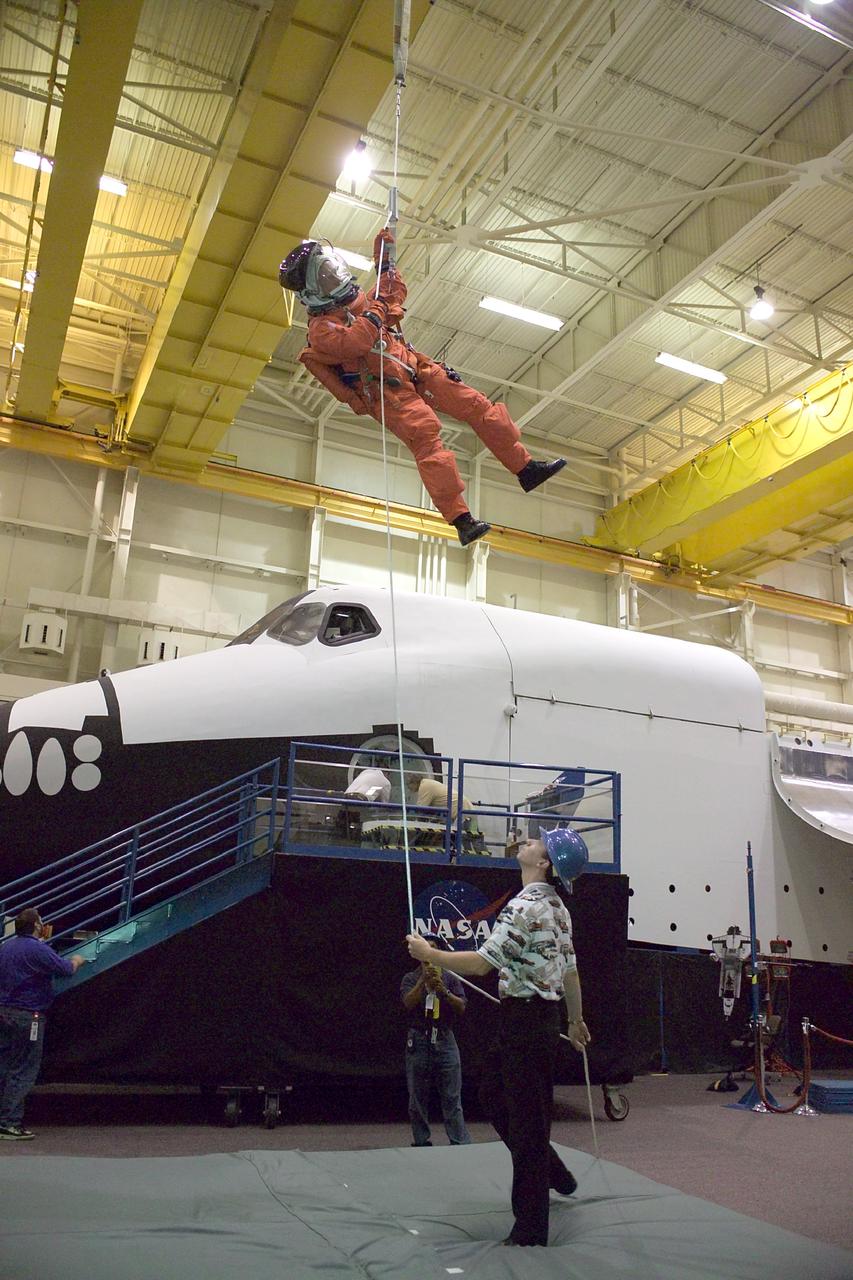 JSC2004-E-37689 (18 August 2004) --- Astronaut Steven W. Lindsey, STS-121 commander, uses a climbing apparatus to lower himself from a simulated trouble-plagued shuttle in an emergency egress training session in the Space Vehicle Mockup Facility at the Johnson Space Center (JSC). Lindsey is wearing a training version of the shuttle launch and entry suit. United Space Alliance (USA) crew trainer David Pogue assisted Lindsey.