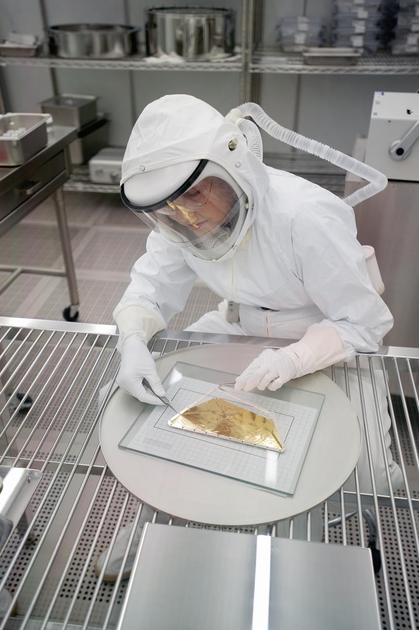 The facility for storing and examining Genesis solar wind samples consists of two adjacent laboratories. In these laboratories, the cutting of gold foil to be used in the gathering of the solar wind dust aboard the Genesis spacecraft. Views include:  The process of cutting gold foil to be used aboard the Genesis spacecraft. The technicians use Gore-Tex suits with filters as to not contaminate the items.