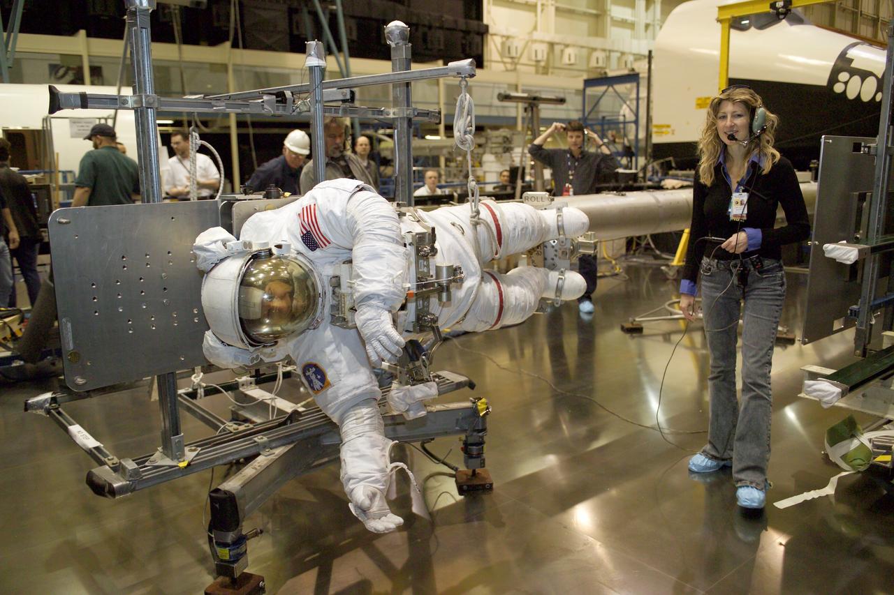 JSC2005-E-08196 (25 February 2005) --- Astronaut Piers J. Sellers, STS-121 mission specialist, wearing a training version of the Extravehicular Mobility Unit (EMU) space suit, participates in an extravehicular activity (EVA) simulation while anchored on the end of the training version of the space shuttle Remote Manipulator System (RMS) robotic arm in the Space Vehicle Mockup Facility at Johnson Space Center. The RMS has a 50-foot boom, called the Orbiter Boom Sensor System (OBSS), extension attached which would be used to reach underneath the orbiter to access tiles. Lora Bailey (right), Manager, JSC Engineering Tile Repair, assisted Sellers.