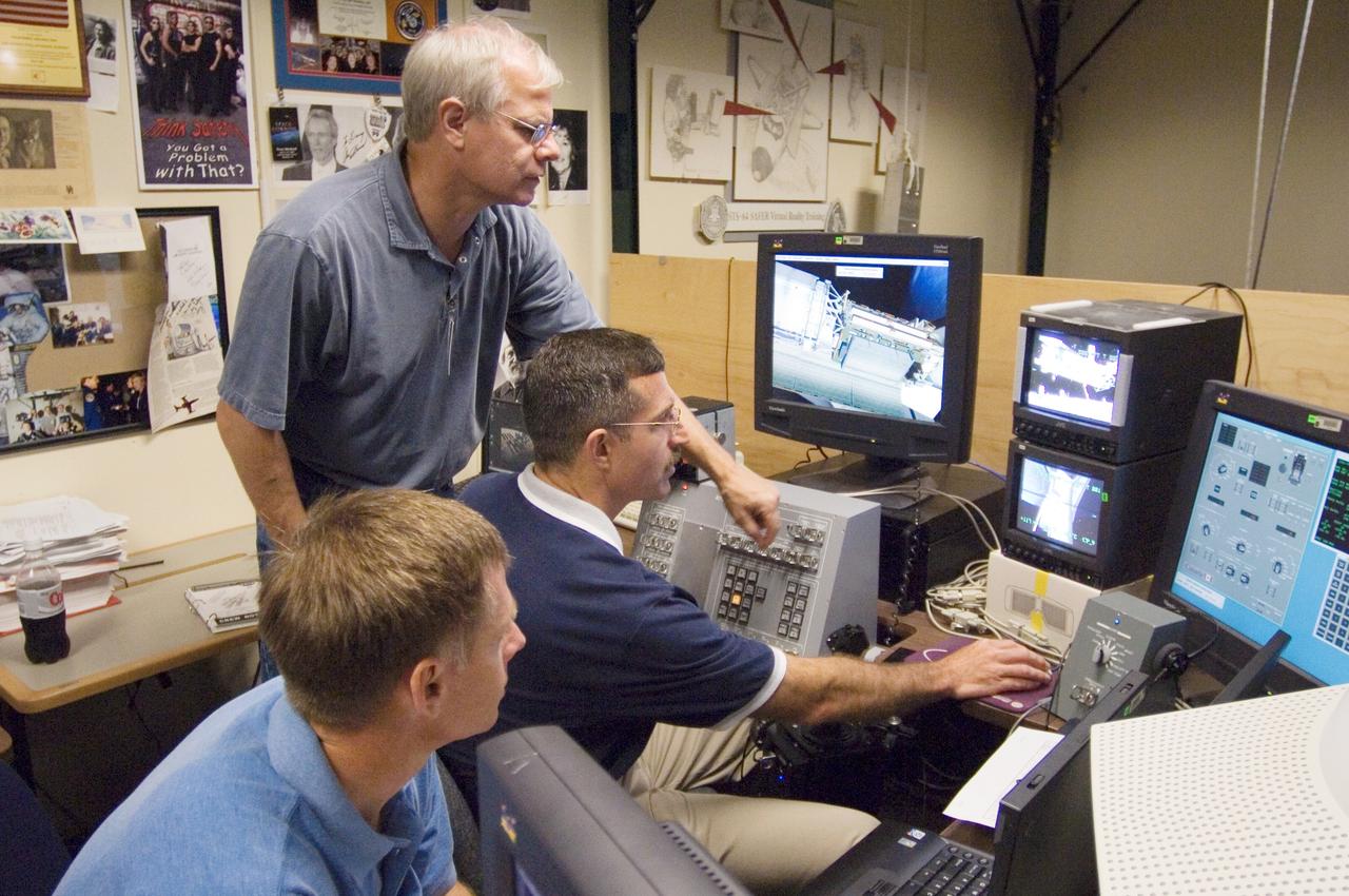JSC2005-E-21199 (7 June 2005) --- Astronaut Daniel C. Burbank, STS-115 mission specialist, uses the virtual reality lab at the Johnson Space Center to train for his duties aboard the space shuttle. This type of computer interface, paired with virtual reality training hardware and software, helps to prepare the entire team for dealing with space station elements. David J. Homan assisted Burbank as astronaut Christopher J. Ferguson, pilot, looked on.
