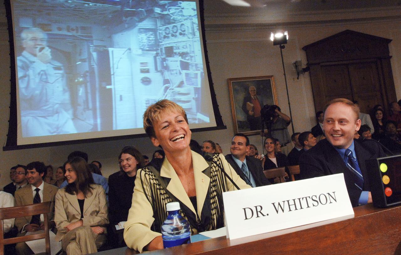 JSC2005-E-22363 (14 June 2005) --- Astronauts Peggy A. Whitson (left) and Edward M. (Mike) Fincke, former Station residents, share a laugh during the House Subcommittee on Space and Aeronautics hearing chaired by Rep. Ken Calvert (R-Calif.), as current Station astronaut John L. Phillips, Expedition 11 NASA ISS science officer and flight engineer, testifies via video screen in the background. Phillips was approximately 220 statute miles above Earth, but his radio transmissions were routed to a Tracking and Data Relay Satellite (TDRS) in geostationary orbit at an altitude of about 22,300 miles. Photo credit: NASA/Bill Ingalls.