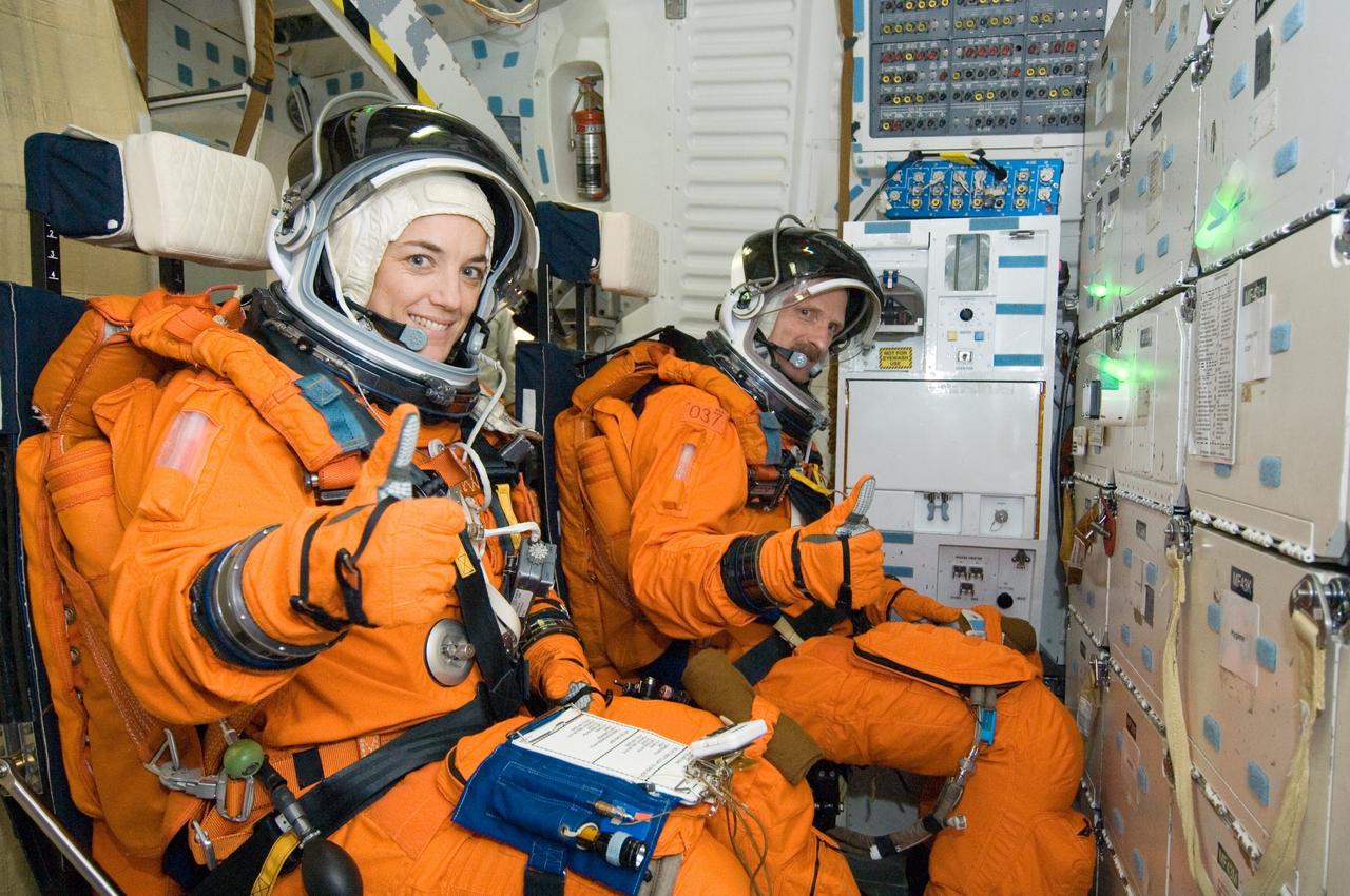 JSC2005-E-47411 (12 Dec. 2005) --- Astronauts Heidemarie M. Stefanyshyn-Piper (foreground) and Joseph R. (Joe) Tanner, both STS-115 mission specialists, give a thumbs-up signal to indicate preparedness for a training session in one of the full-scale trainers in the Space Vehicle Mockup Facility at Johnson Space Center. Attired in training versions of the shuttle launch and entry suit, the two are seated on the middeck for a post insertion training session.