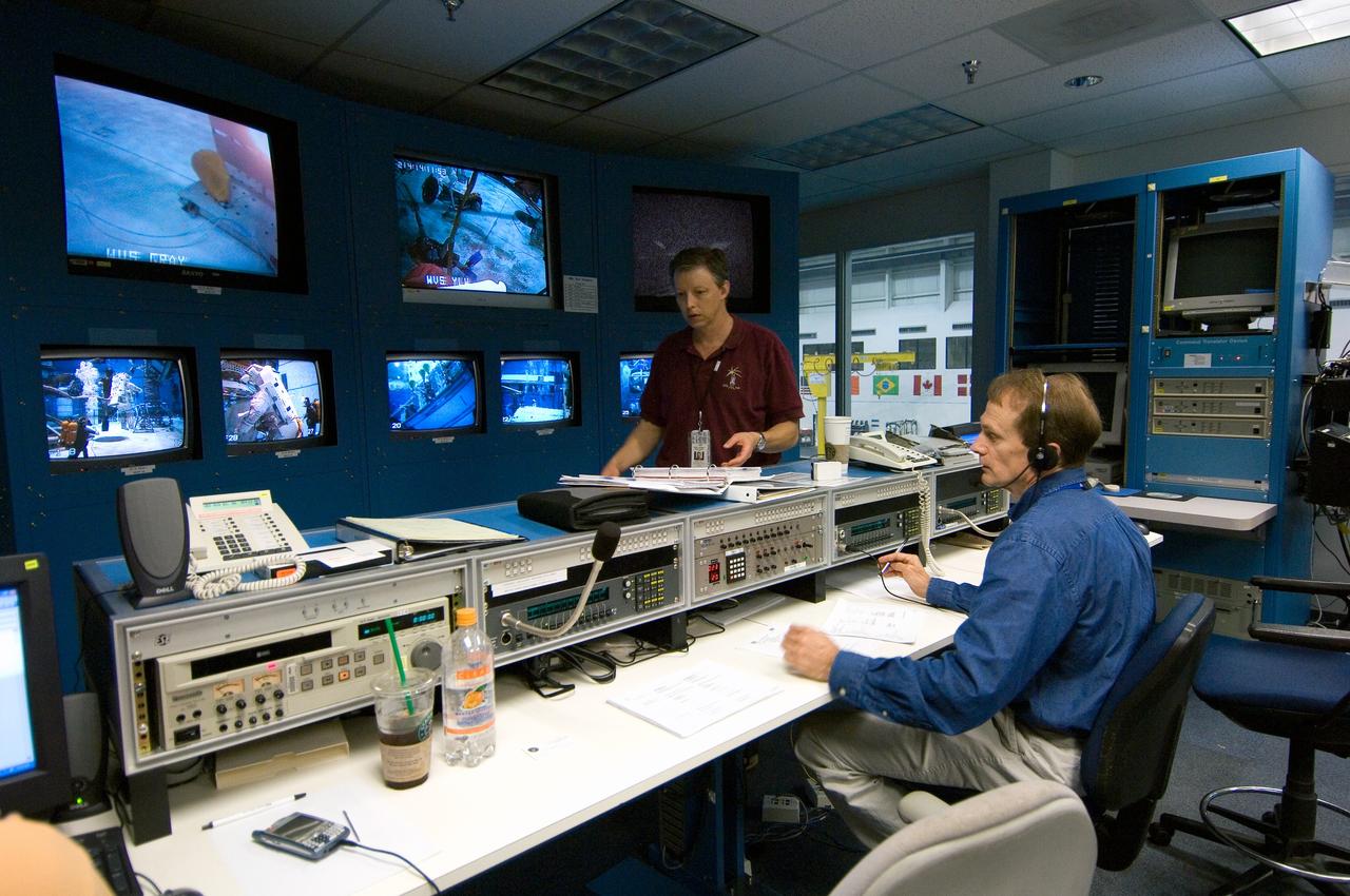 JSC2006-E-31904 (2 Aug. 2006) --- Astronaut Steven G. MacLean (seated), STS-115 mission specialist representing the Canadian Space Agency, observes training activities of his crewmates from the simulation control area in the Neutral Buoyancy Laboratory (NBL) at the Sonny Carter Training Facility (SCTF) near Johnson Space Center. EVA instructor John V. Ray stands nearby to offer assistance.
