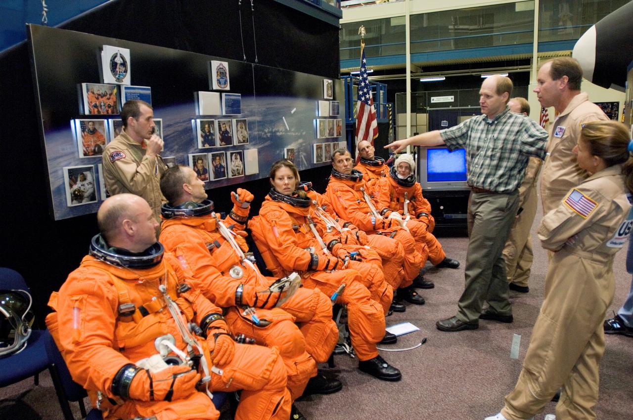 JSC2006-E-43734 (4 Oct. 2006) --- Crew trainer Bob Behrendsen (standing, right background) briefs astronauts Scott J. Kelly (seated left), STS-118 commander; Charles O. Hobaugh, pilot; Tracy E. Caldwell and Richard A. (Rick) Mastracchio, mission specialists; Dafydd R. (Dave) Williams, mission specialist representing the Canadian Space Agency; Barbara R. Morgan, mission specialist; and Clayton C. Anderson, Expedition 15 NASA space station science officer and flight engineer; during a training session in the Space Vehicle Mockup Facility at the Johnson Space Center. The crewmembers are attired in training versions of their shuttle launch and entry suits.