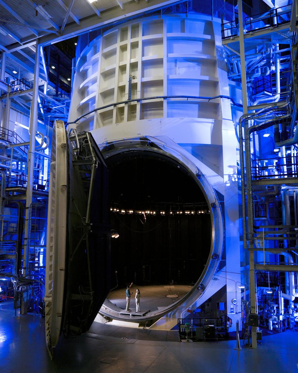 View of Thermal Vacuum Test Chamber A (with it's door opened) in bldg 32.  Two people are standing inside the hatch to show a size comparision.