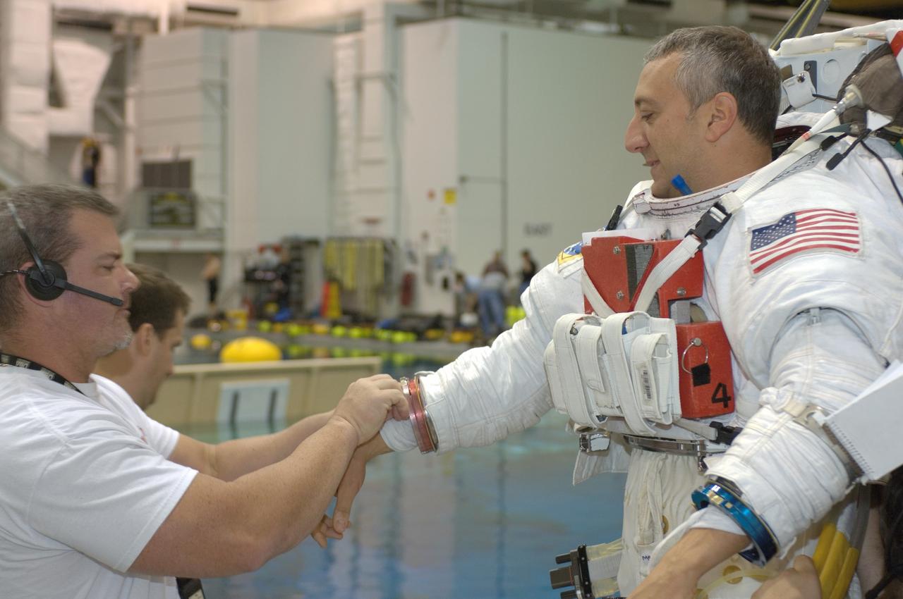JSC2007-E-113591 (18 Dec. 2007) --- Astronaut Michael J. Massimino, STS-125 mission specialist, gets help in the donning of a training version of the Extravehicular Mobility Unit (EMU) spacesuit prior to being submerged in the waters of the Neutral Buoyancy Laboratory (NBL) near the Johnson Space Center.