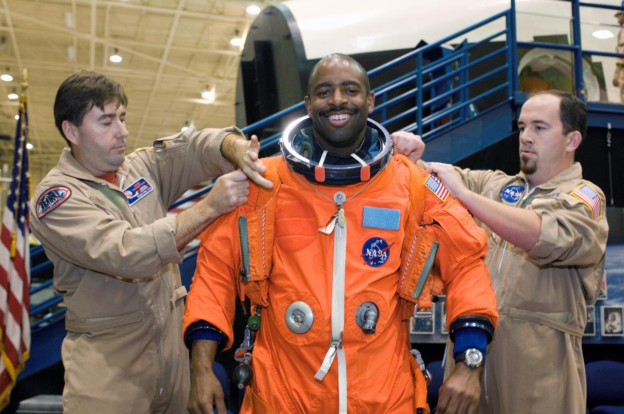 JSC2007-E-14467 (20 March 2007) --- Astronaut Leland D. Melvin, STS-122 mission specialist, dons a training version of his shuttle launch and entry suit in preparation for a post insertion/de-orbit training session in one of the full-scale trainers in the Space Vehicle Mockup Facility at Johnson Space Center. United Space Alliance (USA) suit technicians Mike Thompson (left) and Jeff Chiodo assisted Melvin.