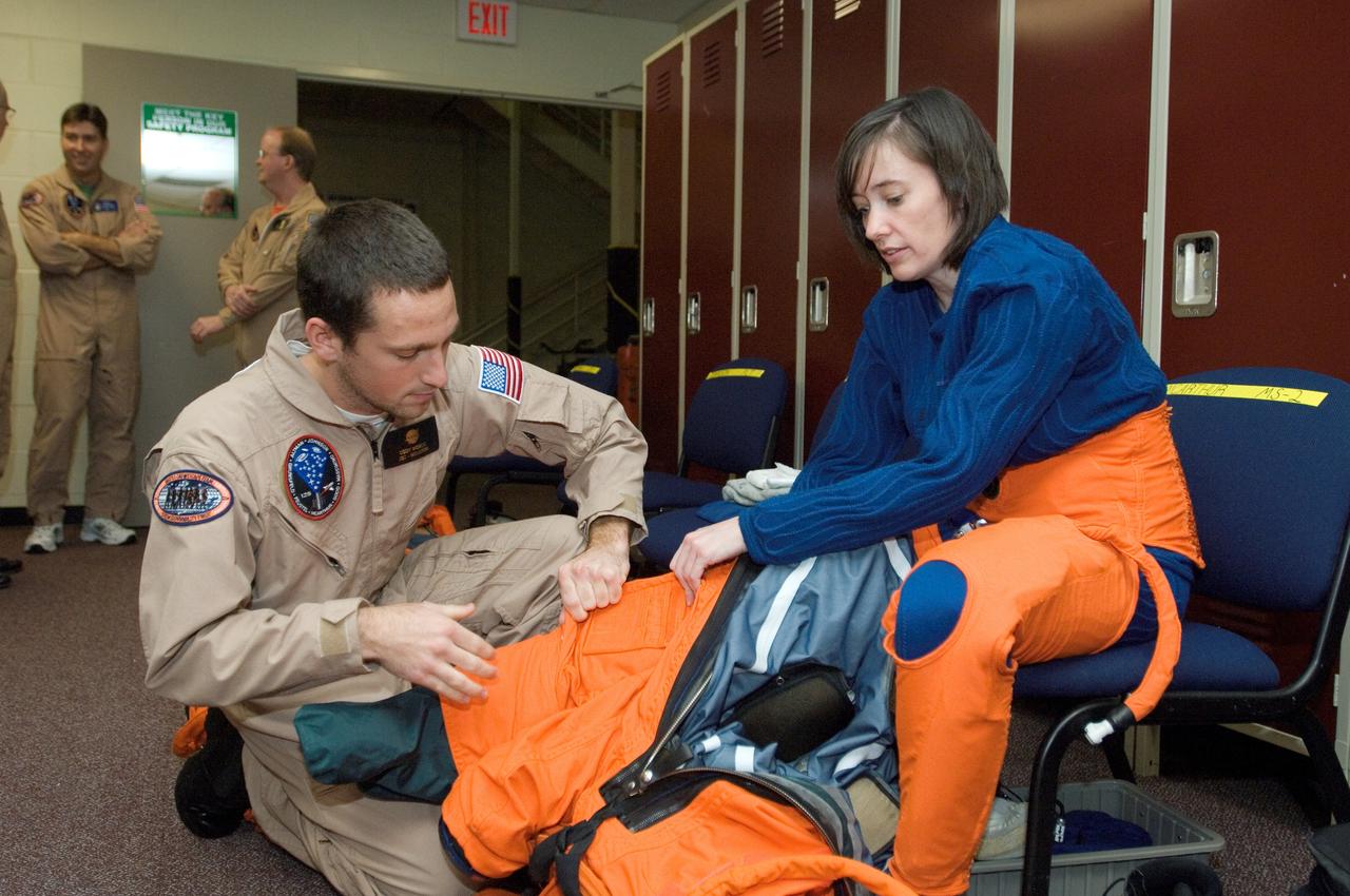 JSC2008-E-018318 (27 Feb. 2008) --- Astronaut K. Megan McArthur, STS-125 mission specialist, dons a training version of her shuttle launch and entry suit in preparation for a training session in the Space Vehicle Mockup Facility at Johnson Space Center. United Space Alliance (USA) suit technician Cody McNeil assisted McArthur.
