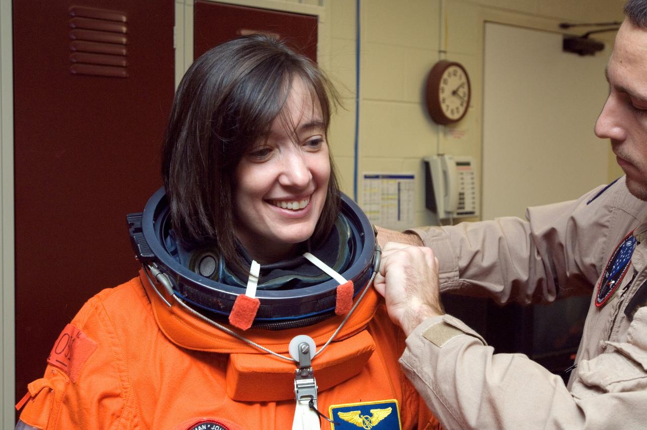 JSC2008-E-018324 (27 Feb. 2008) --- Astronaut K. Megan McArthur, STS-125 mission specialist, dons a training version of her shuttle launch and entry suit in preparation for a training session in the Space Vehicle Mockup Facility at Johnson Space Center. United Space Alliance (USA) suit technician Cody McNeil assisted McArthur.