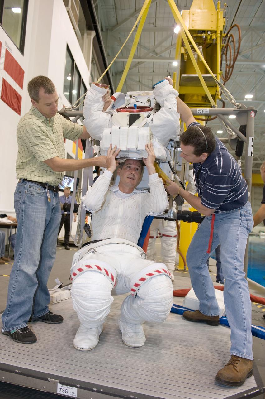 JSC2008-E-118357 (25 Sept. 2008) --- Astronaut Michael Good, STS-125 mission specialist, dons a training version of his Extravehicular Mobility Unit (EMU) space suit in preparation for a training session in the waters of the Neutral Buoyancy Laboratory (NBL) near NASA's Johnson Space Center. Astronaut Andrew Feustel (left), mission specialist, and United Space Alliance suit technician Beau Webb (right) assisted Good.