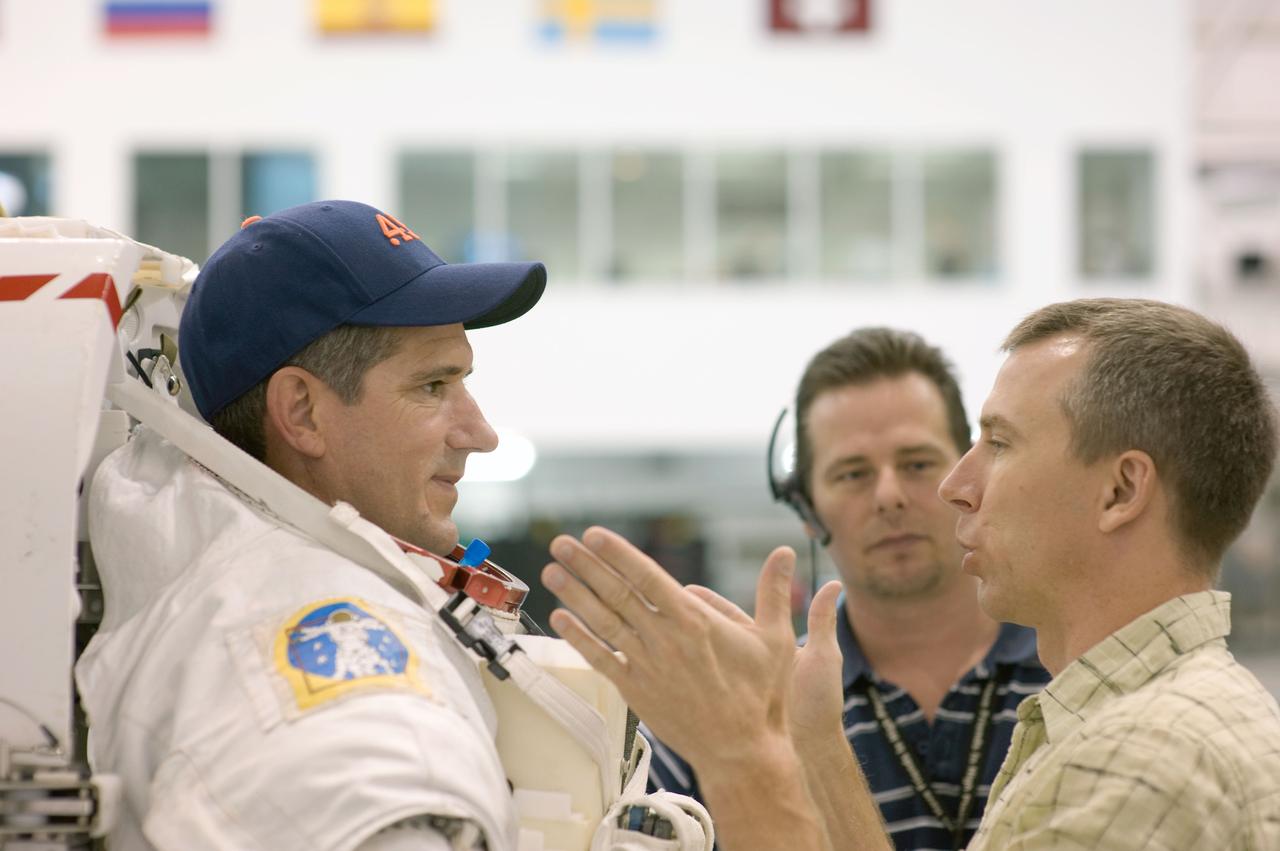 JSC2008-E-118360 (25 Sept. 2008) --- Astronauts Michael Good (left) and Andrew Feustel, both STS-125 mission specialists, discuss training activities in the Neutral Buoyancy Laboratory (NBL) near NASA's Johnson Space Center. Good is wearing a training version of his Extravehicular Mobility Unit (EMU) spacesuit. United Space Alliance suit technician Beau Webb is visible at center.