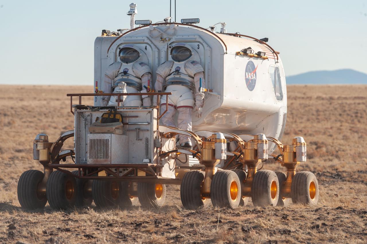 A back view of the Lunar Electric Rover (LER) during the Desert Research and Technology Studies (RATS) remote field test at Black Point Lava Flow, Arizona in 2008. Two Mark III spacesuits are visibly mounted on the LER suit port.