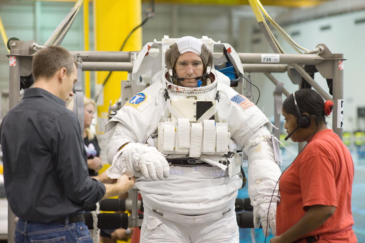 JSC2008-E-141519 (6 Nov. 2008) --- Astronaut Michael Good, STS-125 mission specialist, dons a training version of his Extravehicular Mobility Unit (EMU) spacesuit prior to being submerged in the waters of the Neutral Buoyancy Laboratory (NBL) near NASA's Johnson Space Center. Astronaut Andrew Feustel, mission specialist, assisted Good.