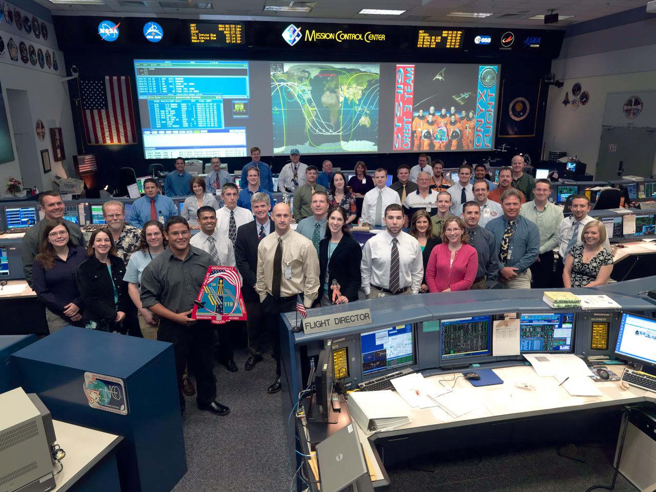 JSC2009-E-061542 (24 March 2009) --- The members of the STS-119 Orbit 3 flight control team pose for a group portrait in the space shuttle flight control room in the Mission Control Center at NASA?s Johnson Space Center. Flight director Bryan Lunney (center) near the front.