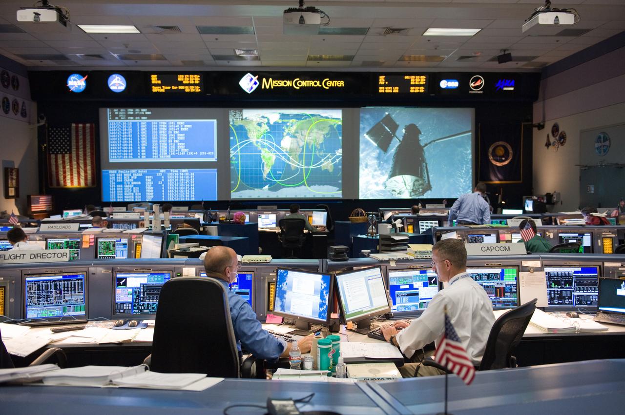 JSC2009-E-119746 (13 May 2009) --- Flight director Tony Ceccacci (left) and astronaut Dan Burbank, STS-125 spacecraft communicator (CAPCOM), monitor data at their consoles in the space shuttle flight control room in the Mission Control Center at NASA's Johnson Space Center during flight day three activities. The Hubble Space Telescope, grappled by Space Shuttle Atlantis? remote manipulator system (RMS), is visible on one of the big screens.