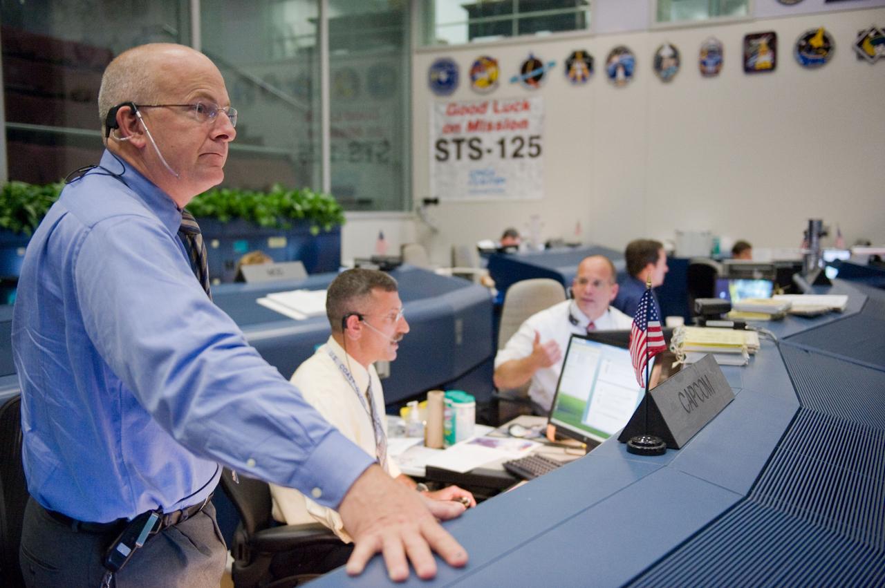 JSC2009-E-120487 (14 May 2009) --- Astronauts Alan Poindexter (standing) and Dan Burbank (seated left), STS-125 spacecraft communicators (CAPCOM); along with flight director Tony Ceccacci are pictured at their consoles in the space shuttle flight control room in the Mission Control Center at NASA's Johnson Space Center during flight day four activities.